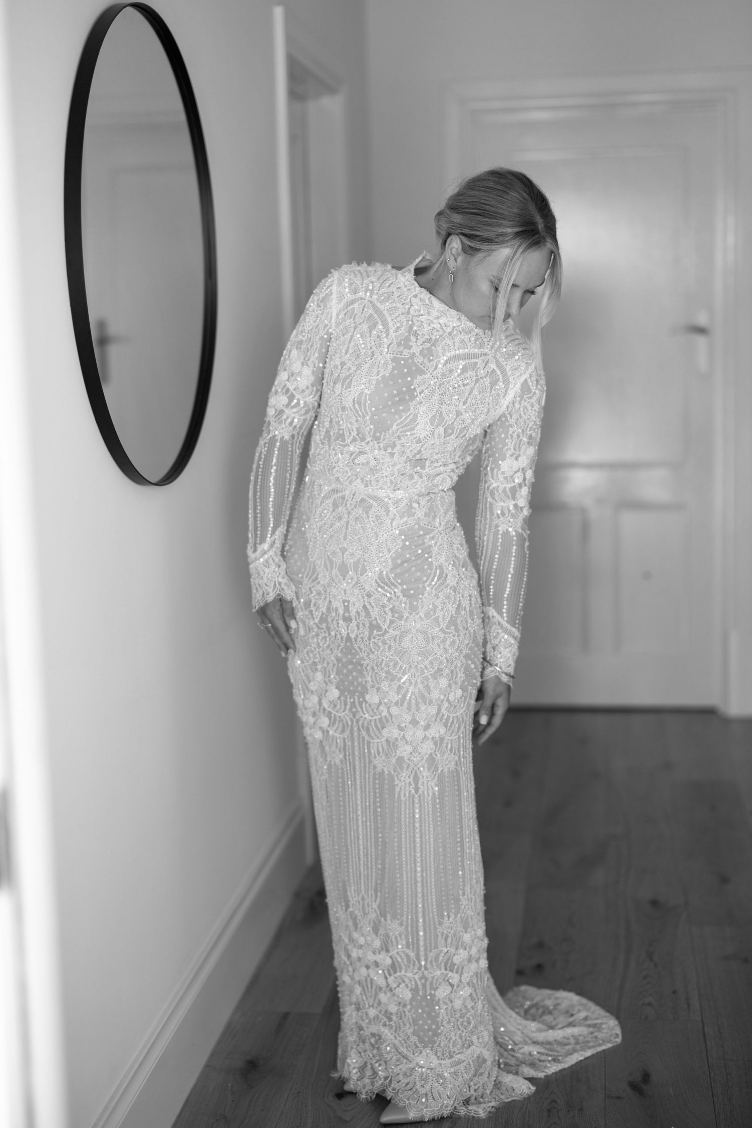 Bride in long-sleeve beaded lace wedding gown posing elegantly in black and white photo.