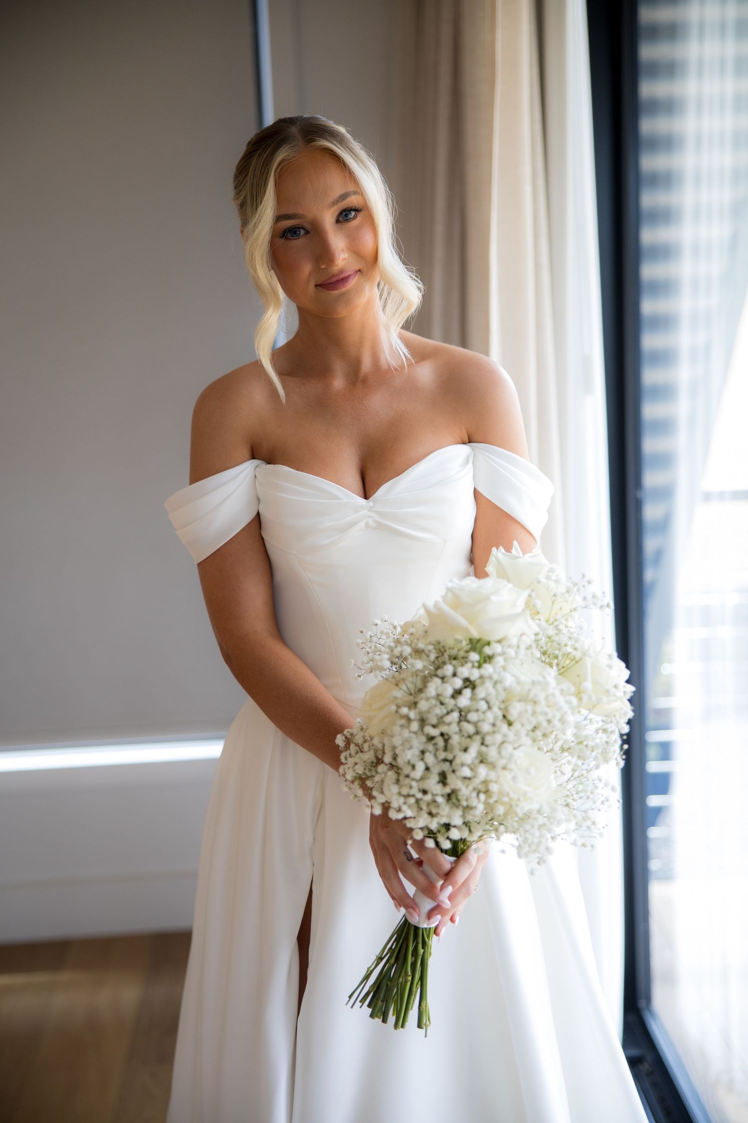 Beautiful bride holding white rose and baby's breath bouquet in an off-shoulder wedding dress.
