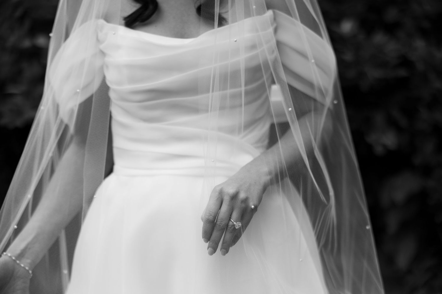 Black and white photo of a bride in a elegant wedding gown with veil, showcasing her diamond ring.