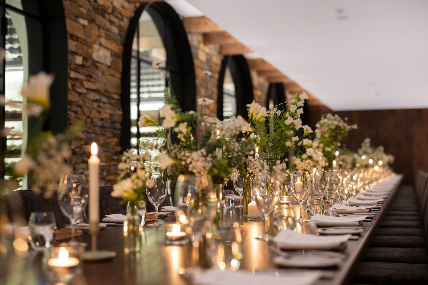 Elegant wedding reception table with candles and floral arrangements in a stone-walled venue.