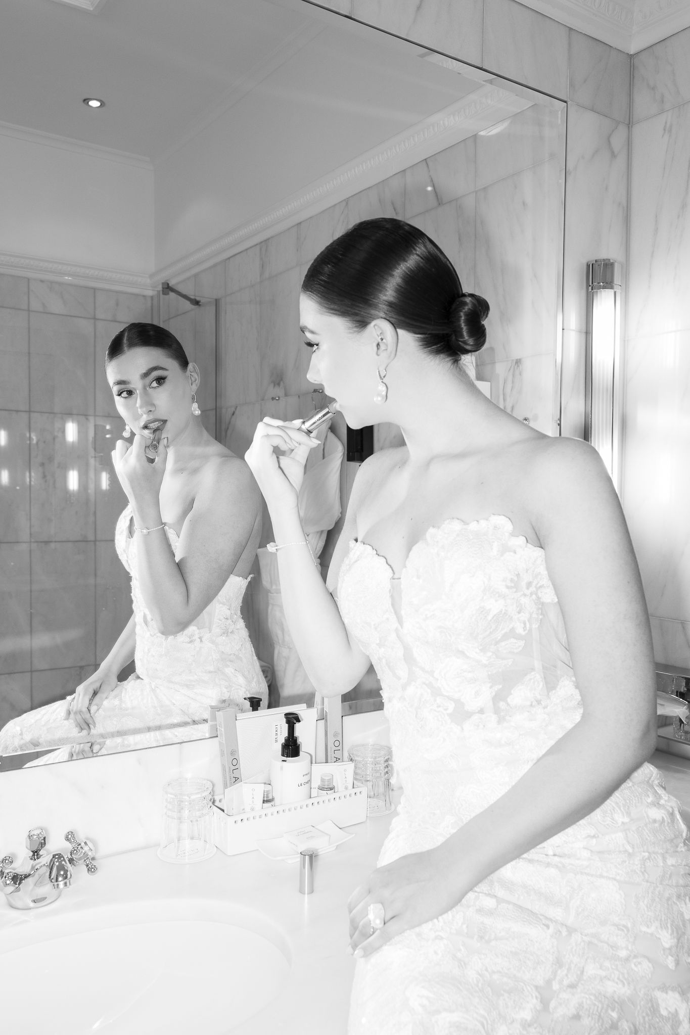 Black and white photo of bride in strapless lace gown applying lipstick at bathroom mirror.Fashion bridal in Vienna.