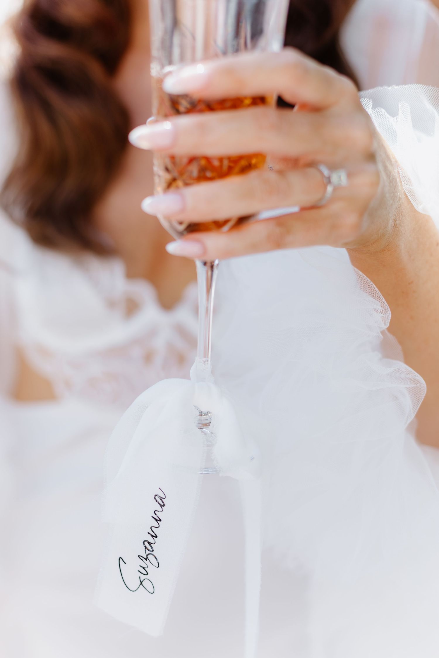 Bride holding a champagne flute with a personalized name tag reading Susanna at a wedding celebration.