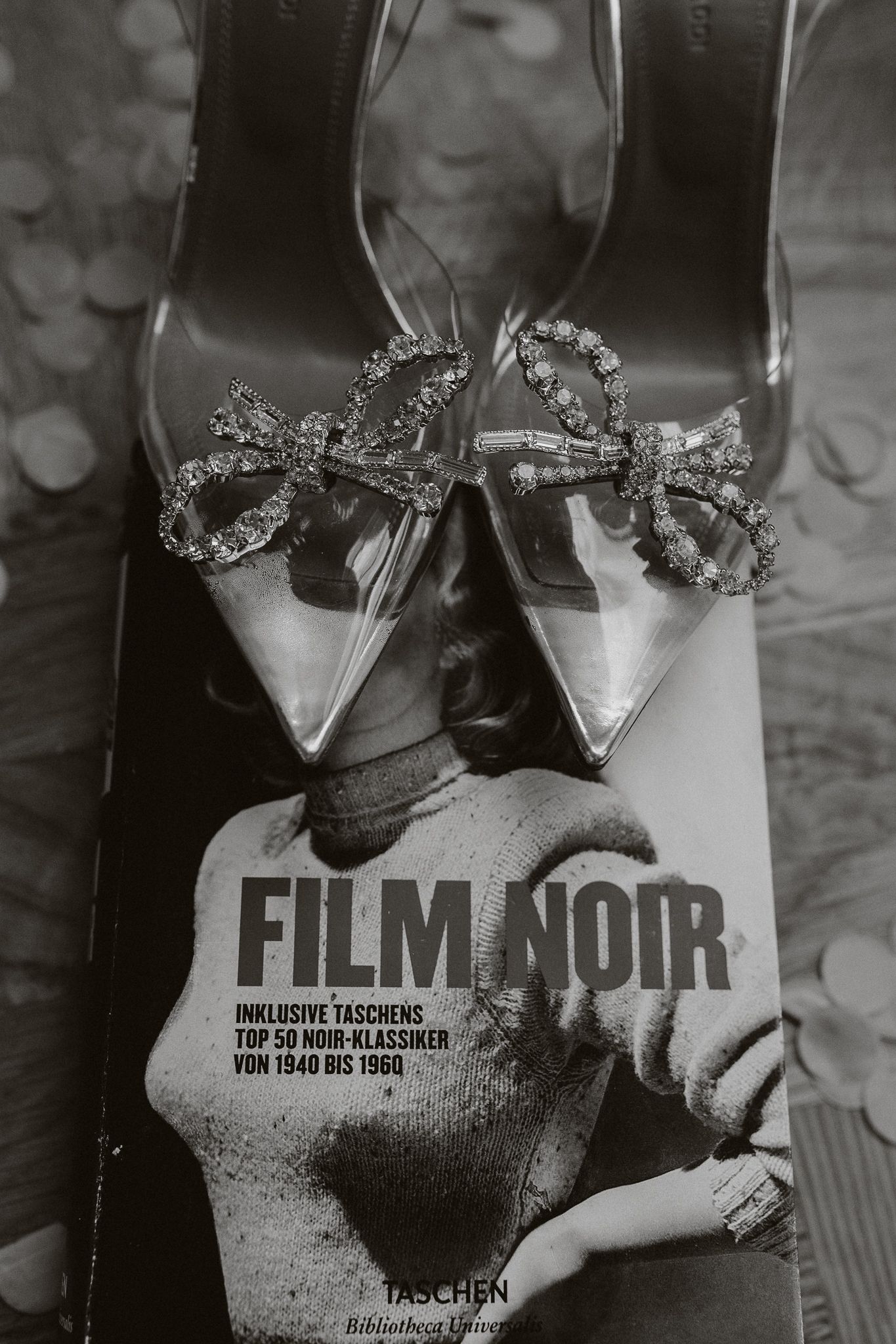 Crystal bow heels resting on a Film Noir Taschen book in black and white photography.