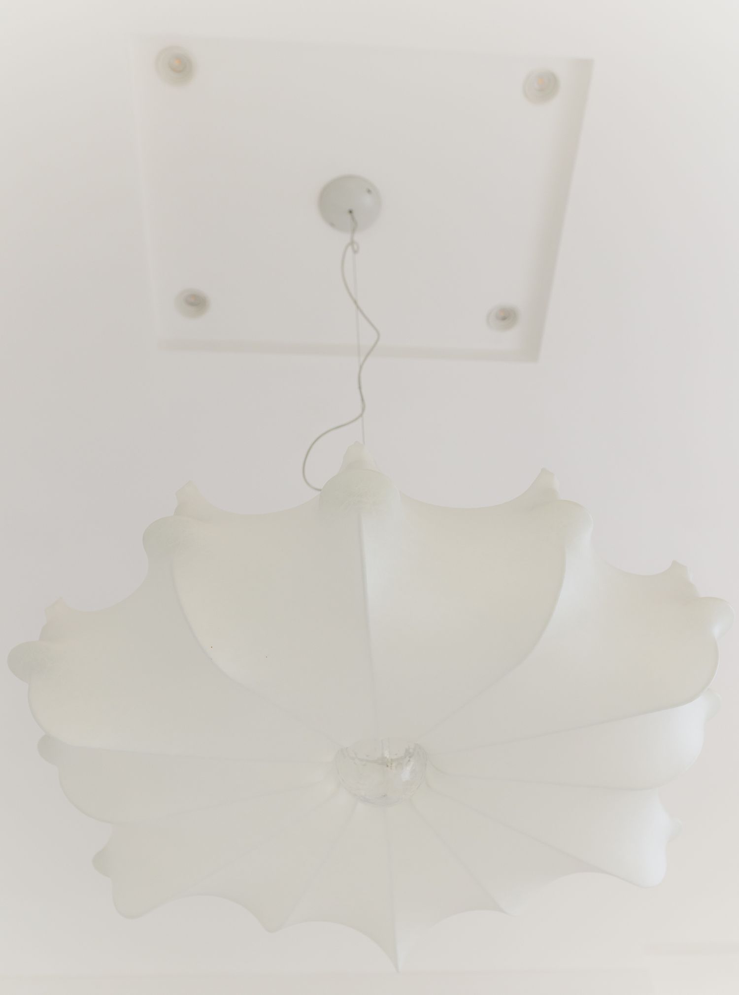 White flower-shaped ceiling light pendant hanging from square ceiling mount in bright white room.