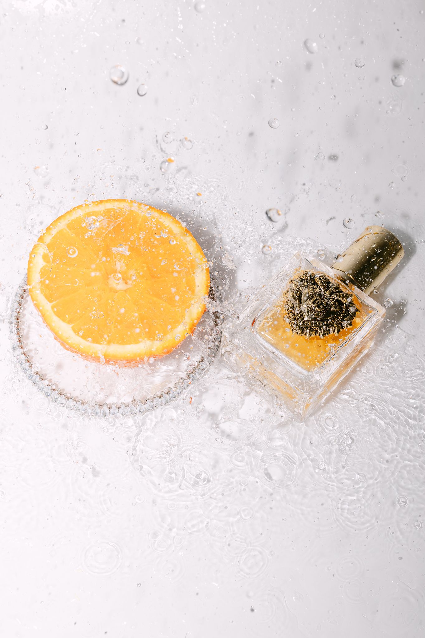 Orange slice and serum bottle submerged in water with bubbles on white background.