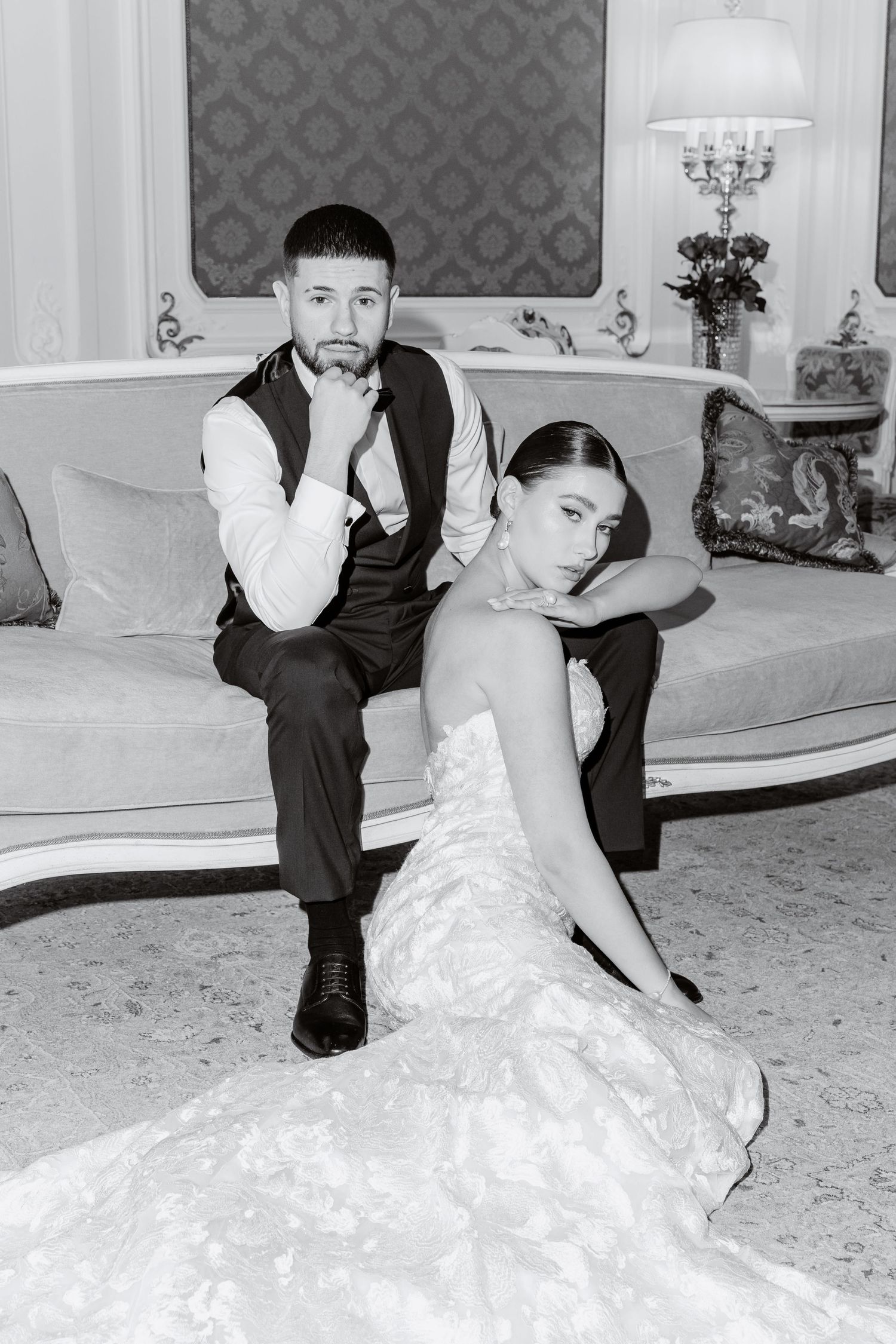 Bride and groom posing together on sofa in classic interior in black and white portrait.