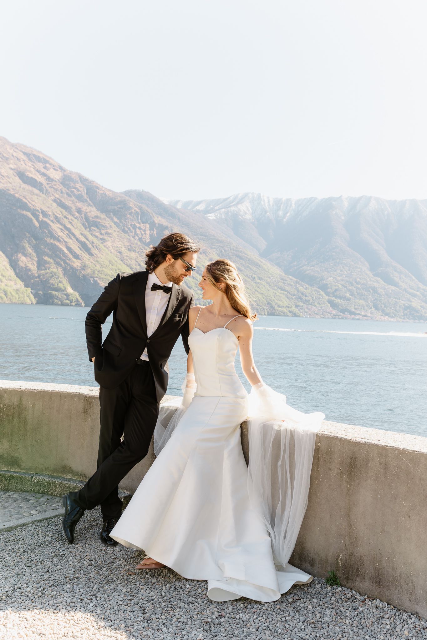 Romantic couple in wedding attire sharing tender moment overlooking scenic lake and mountains.