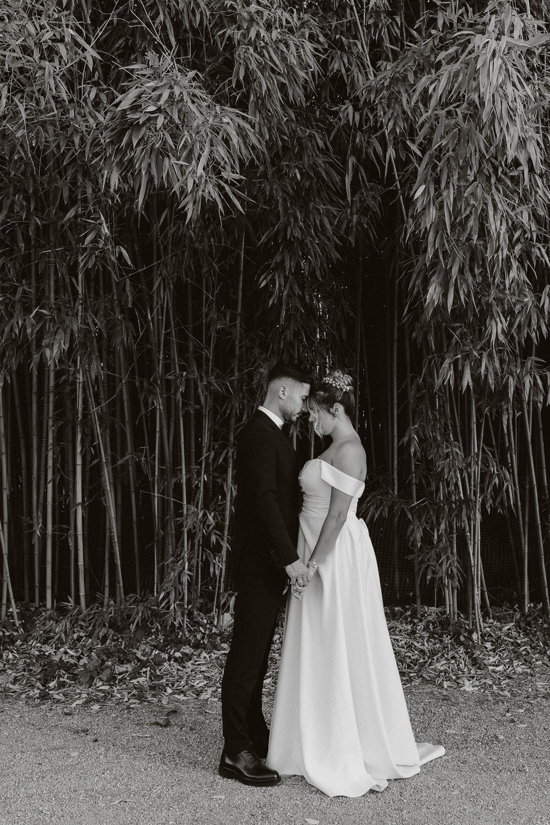 Bride and groom holding hands facing each other before a lush bamboo grove.