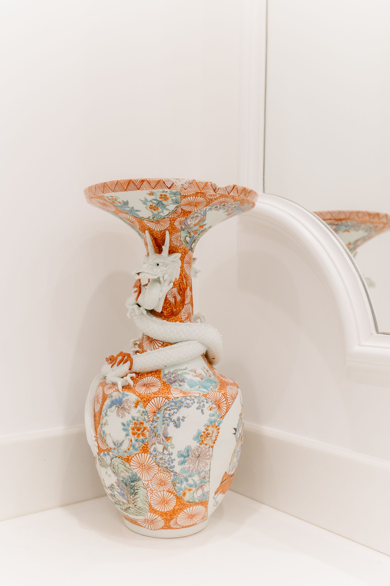 Ornate Japanese Imari porcelain vase with dragon motif in orange, white, and teal on white shelf.