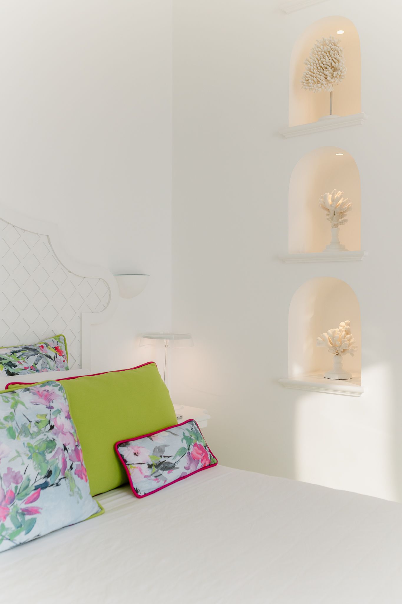 White bedroom with floral and green pillows and illuminated arched wall niches with decor.