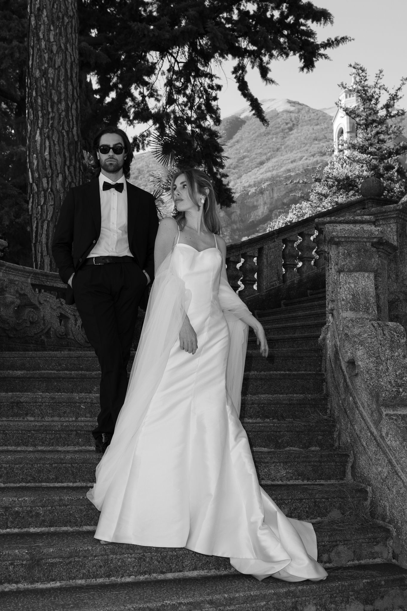 Black and white wedding portrait of bride and groom descending ornate stone stairs at a villa.