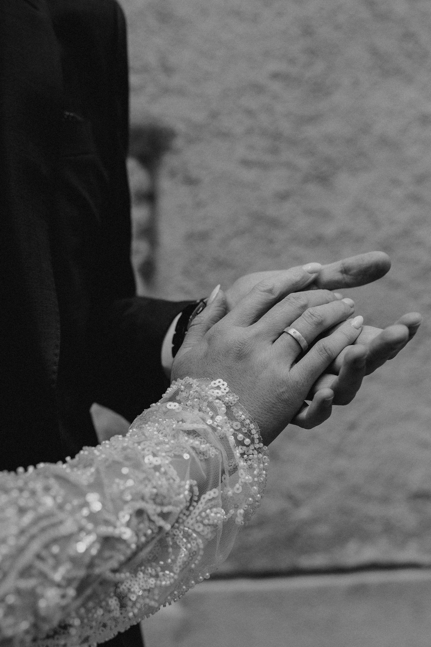 Black and white close-up of bride and groom holding hands showing wedding rings.