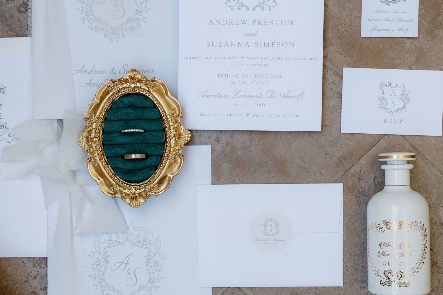 Elegant wedding invitation suite with gold ornate ring box, white envelopes, and monogram wax seal on marble surface.