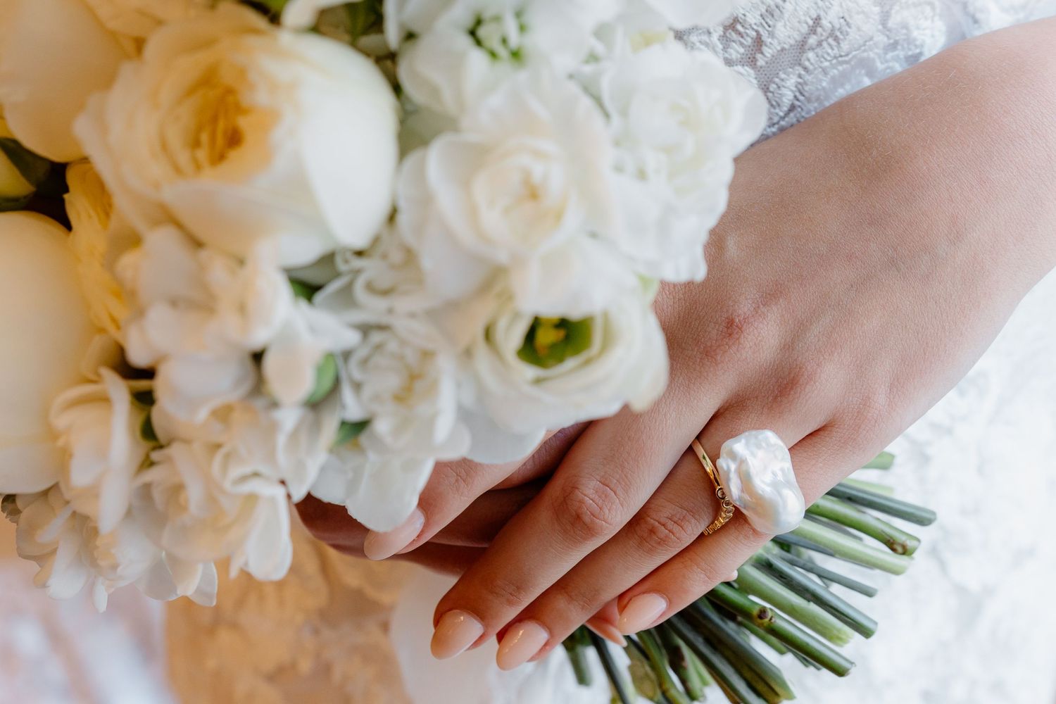 Bride holding white rose bouquet with gold ring on finger at wedding.
