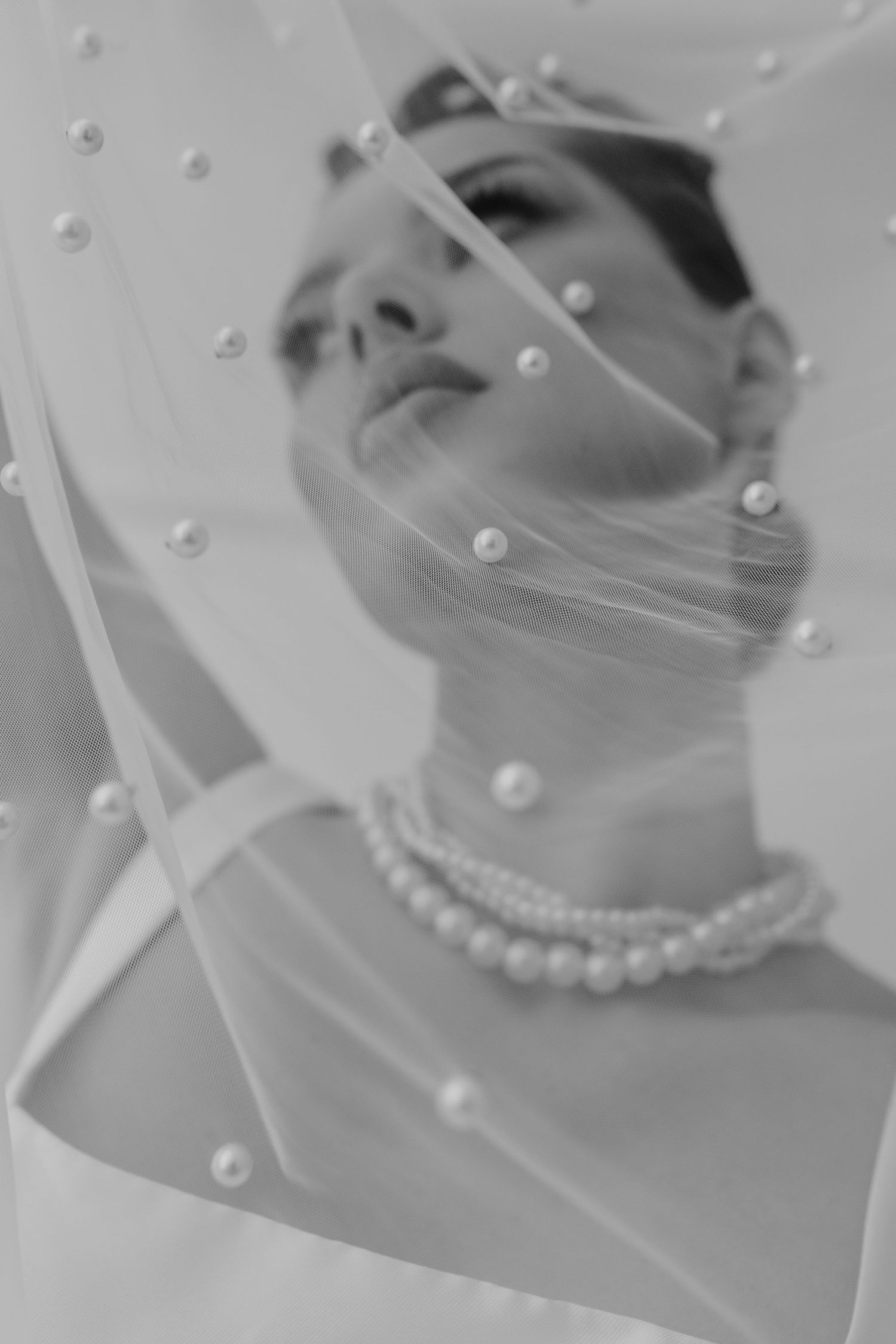 Bride wearing pearl necklace and veil with pearl accents in black and white portrait photography.