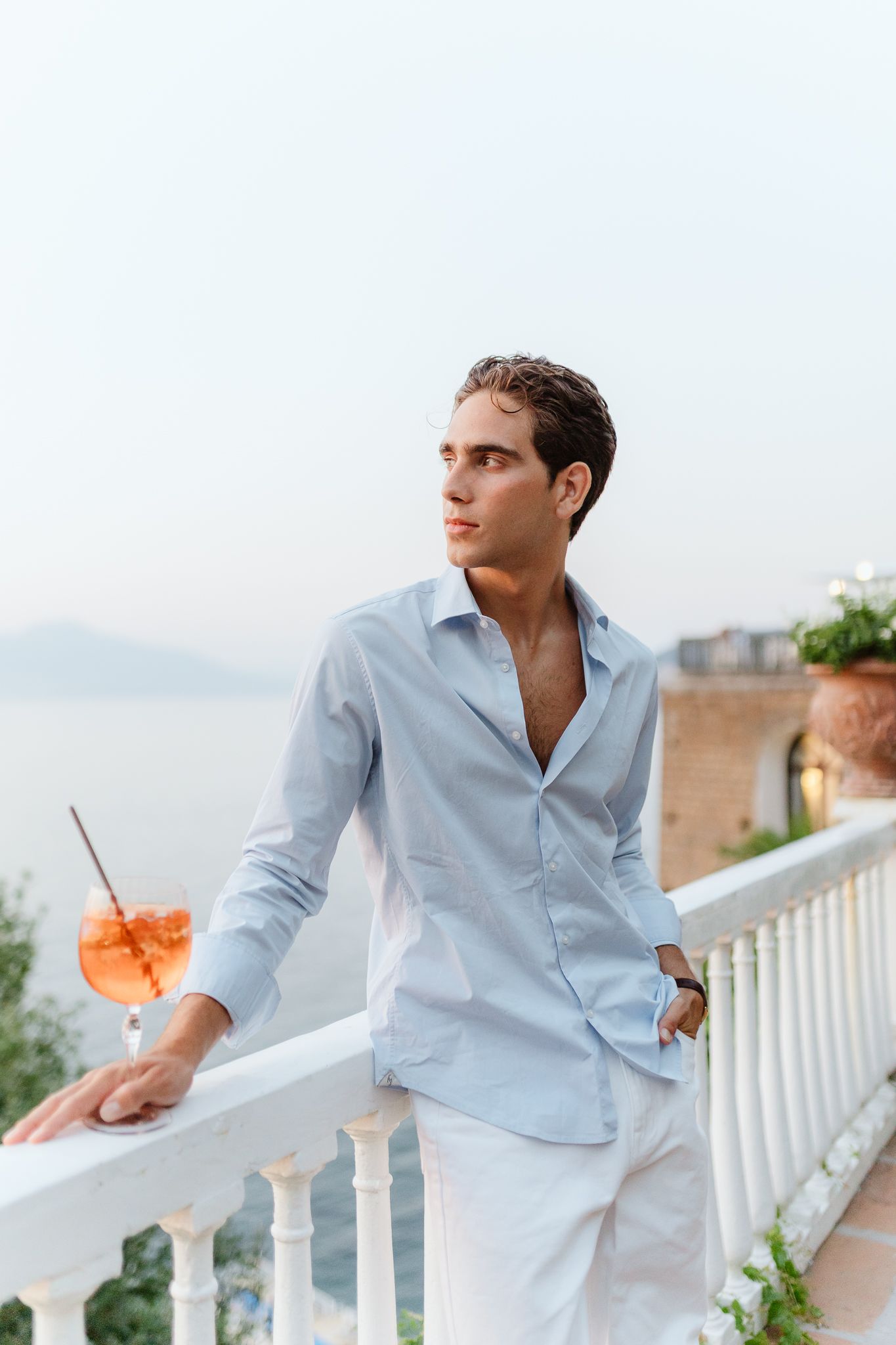 Handsome man in light blue shirt with cocktail on scenic seaside terrace at Villa Silvana terrace.