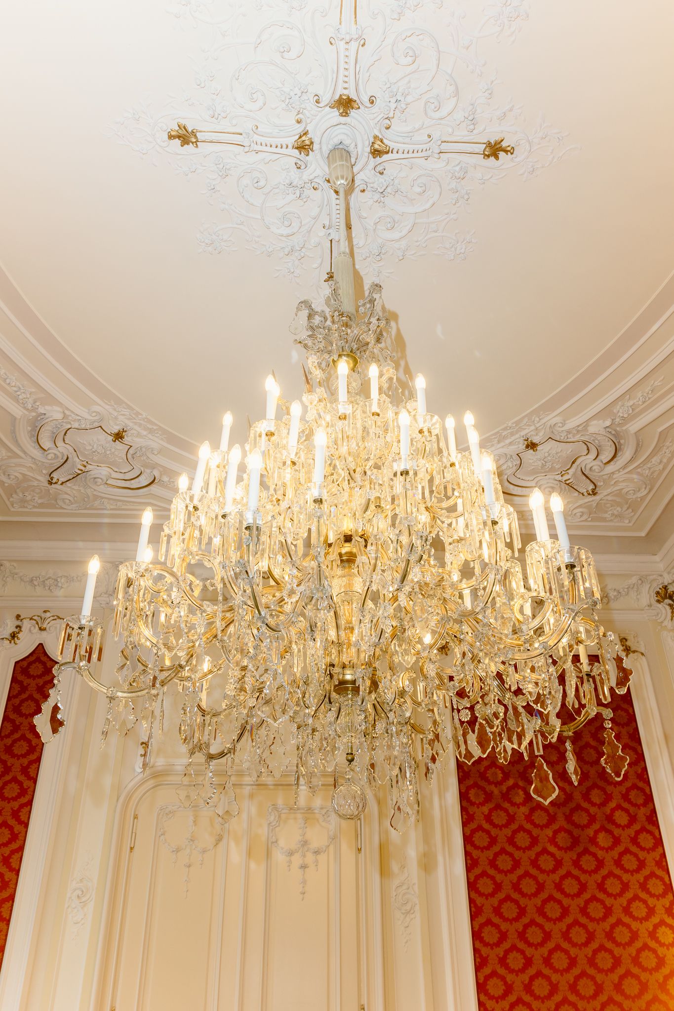 Magnificent crystal chandelier with lit candle-style lights hanging from ornate white plaster ceiling medallion.