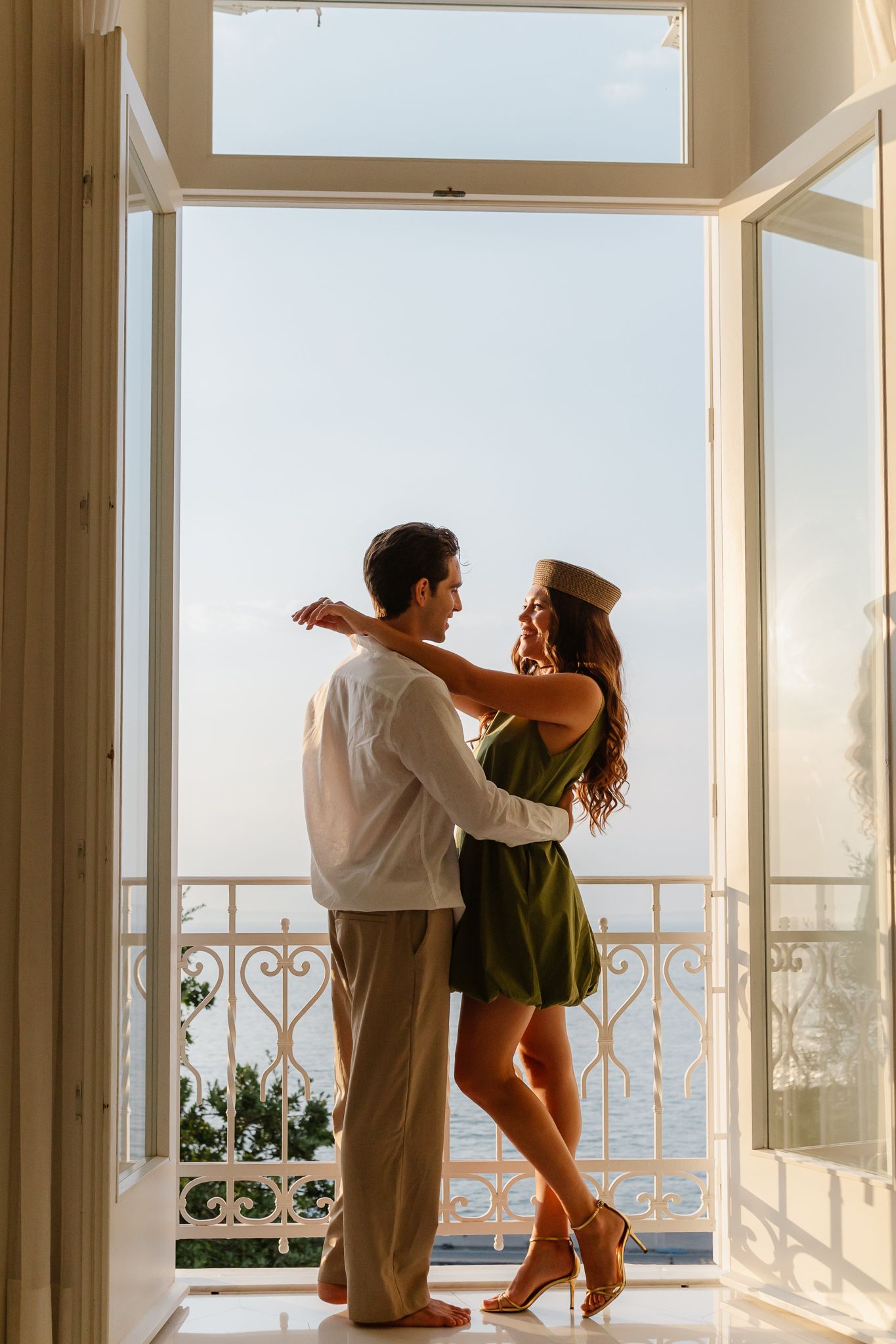 Couple embracing in open balcony doorway with scenic ocean view at golden hour.