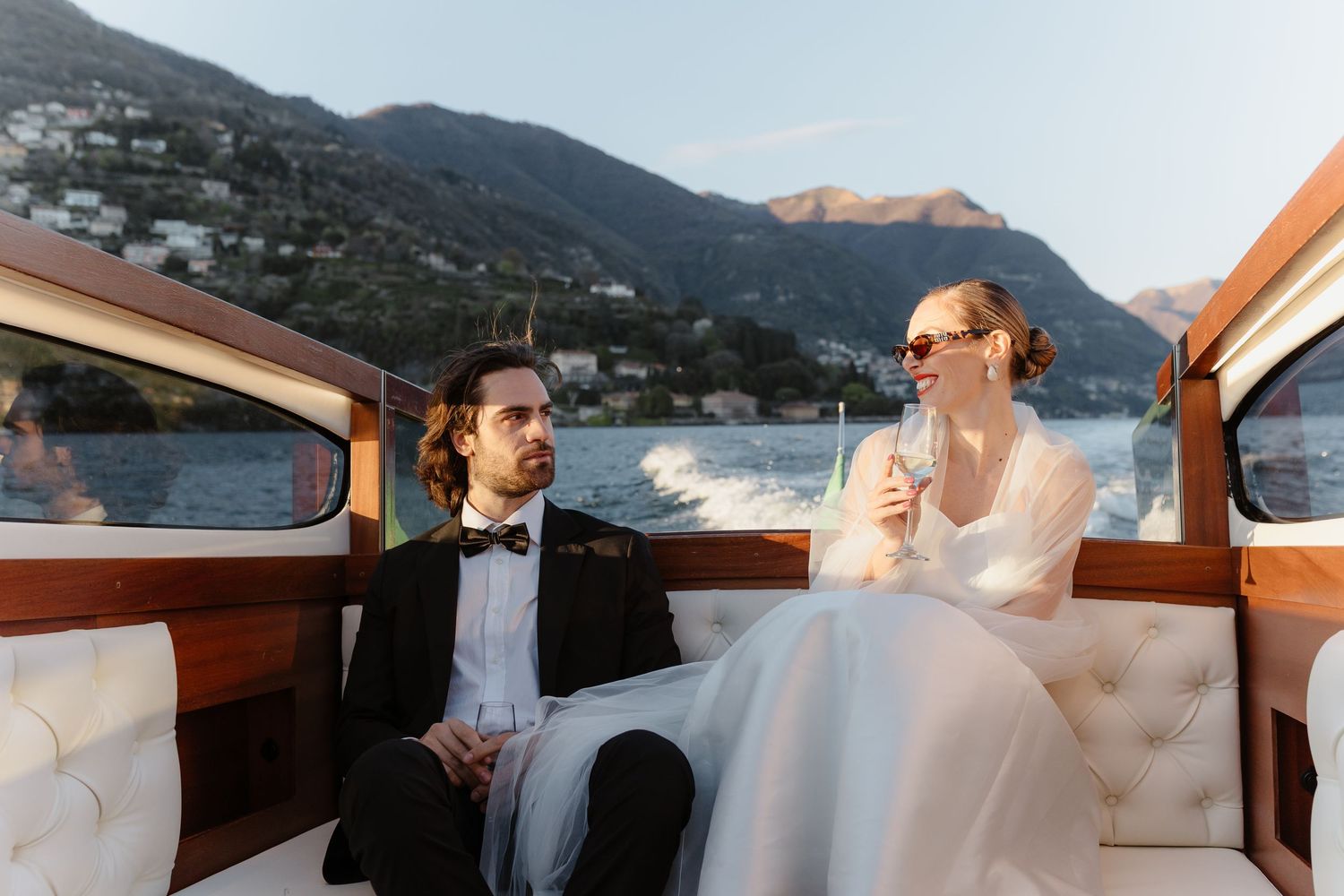 Bride and groom sitting together on a luxury boat with stunning Lake Como mountain backdrop.