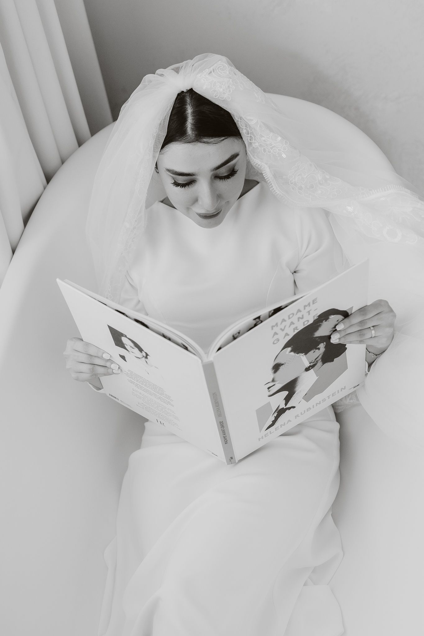 Elegant bride in wedding dress and veil reading magazine while relaxing in bathtub.