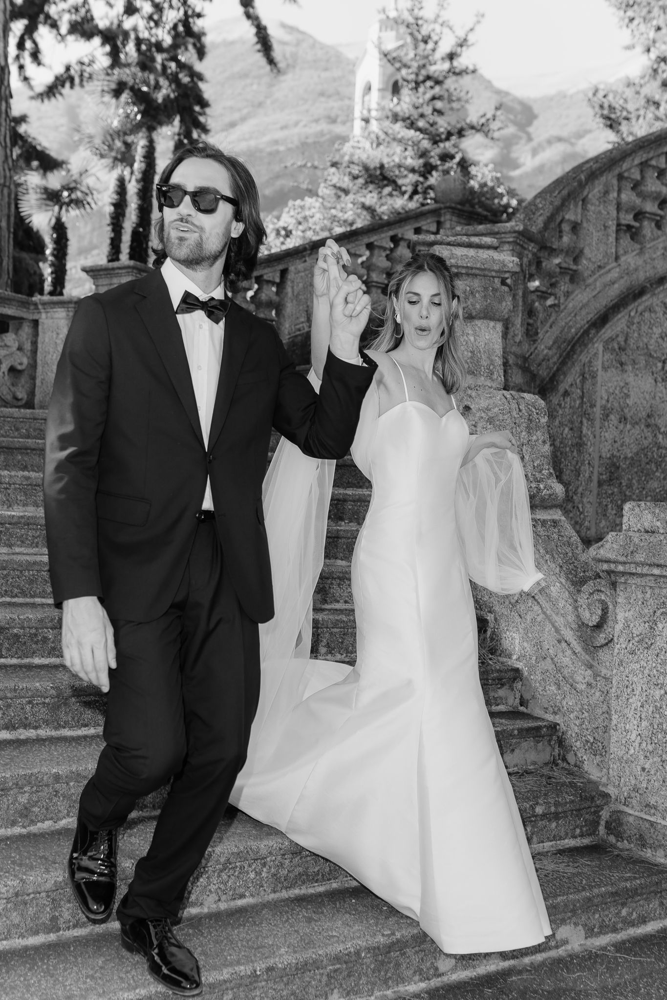 Black and white photo of groom leading bride by hand down grand stone staircase at Italian villa.