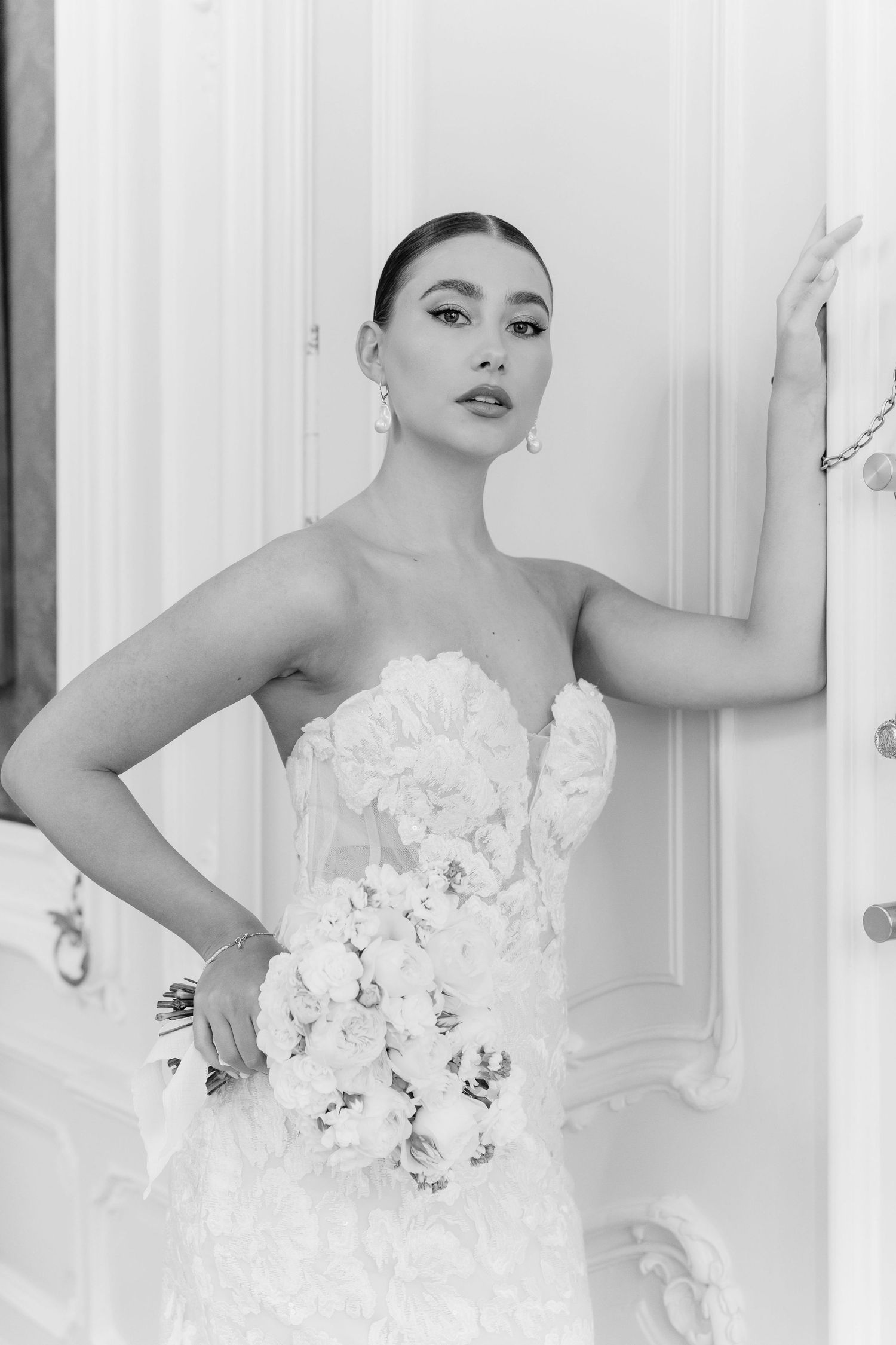 Elegant bride in strapless floral wedding gown holding bouquet in black and white portrait.