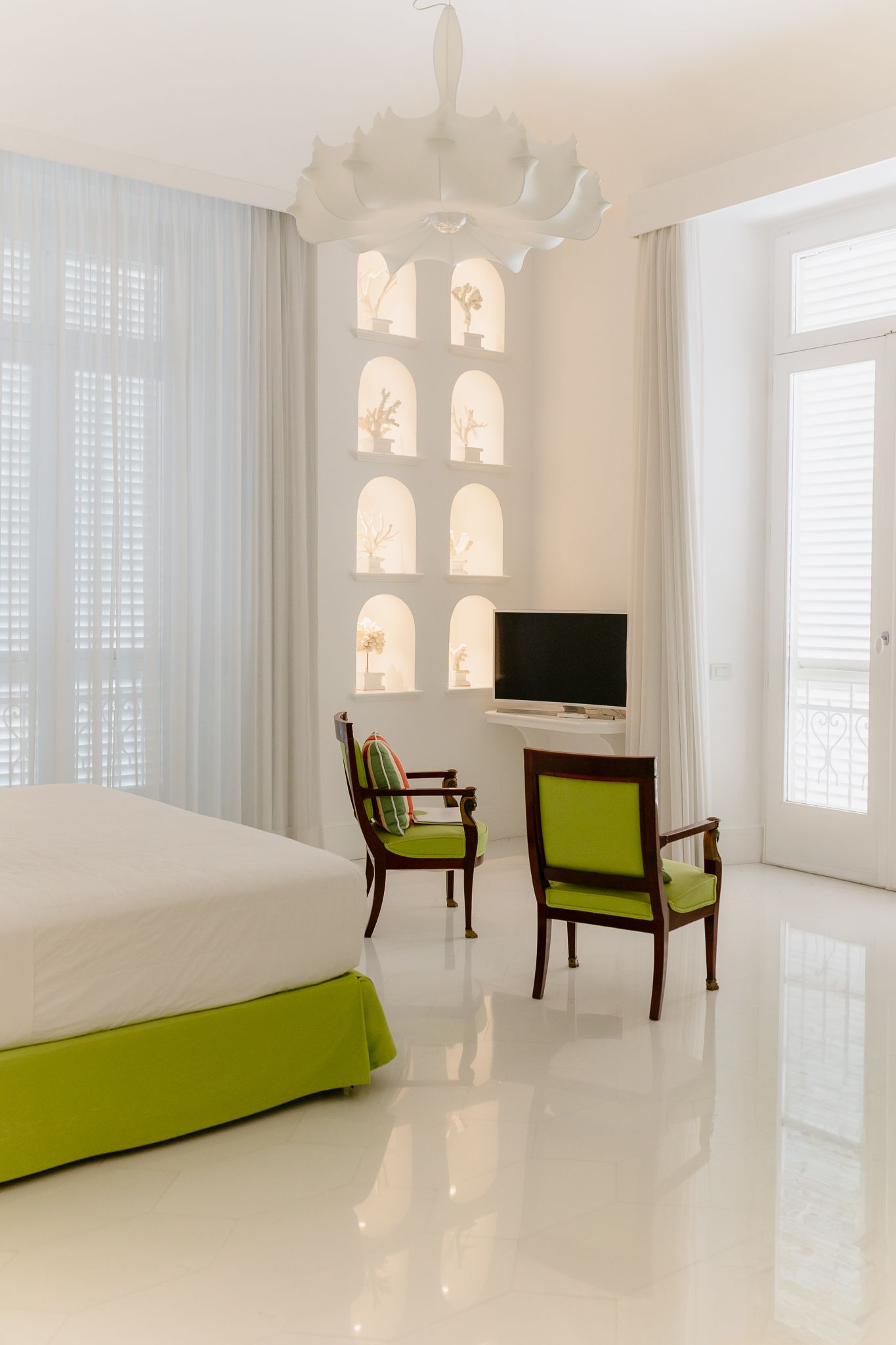 Bright white hotel room with green accents, arched display niches, and balcony view.