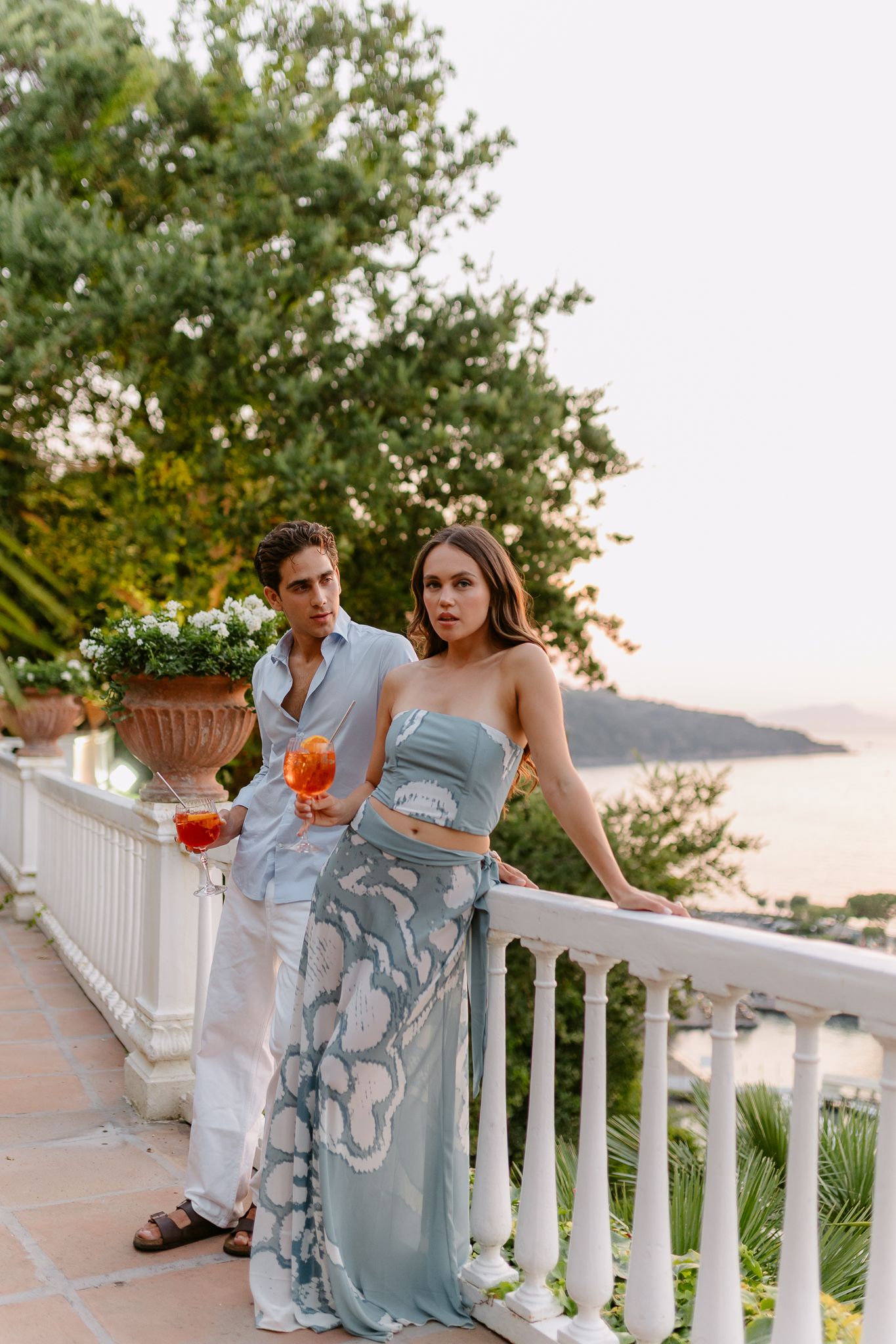 Elegant couple posing on a luxury terrace with cocktails and ocean views at sunset in Sorrento,Italy.
