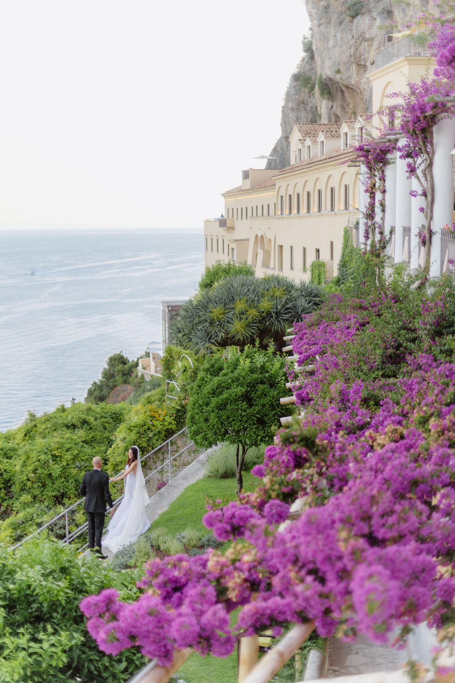 Bride and groom stroll along terraced gardens  overlooking the Amalfi Coast sea.Celebrate destination wedding in Italy.