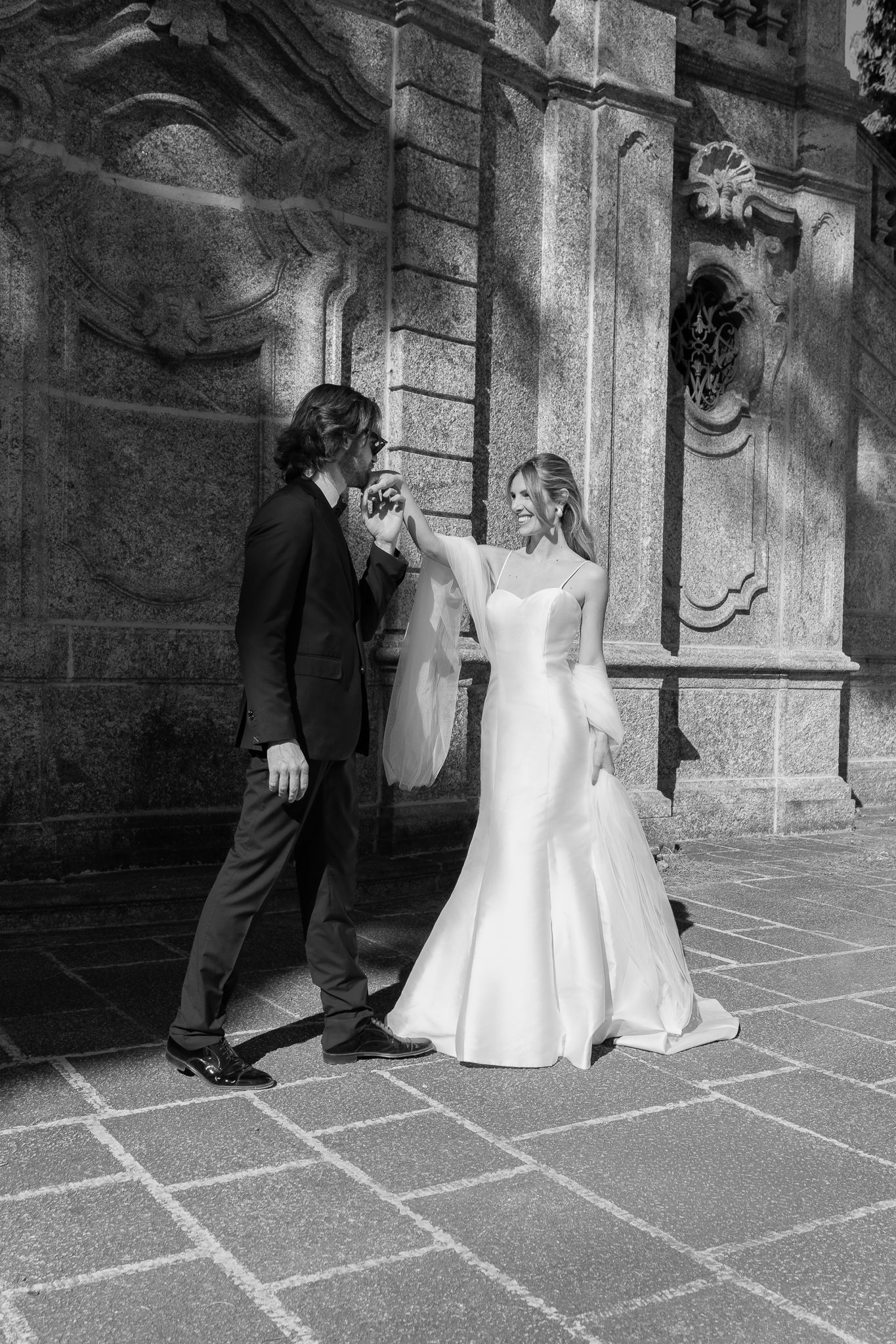 Black and white photo of a bride and groom dancing outside an ornate stone building on their wedding day.