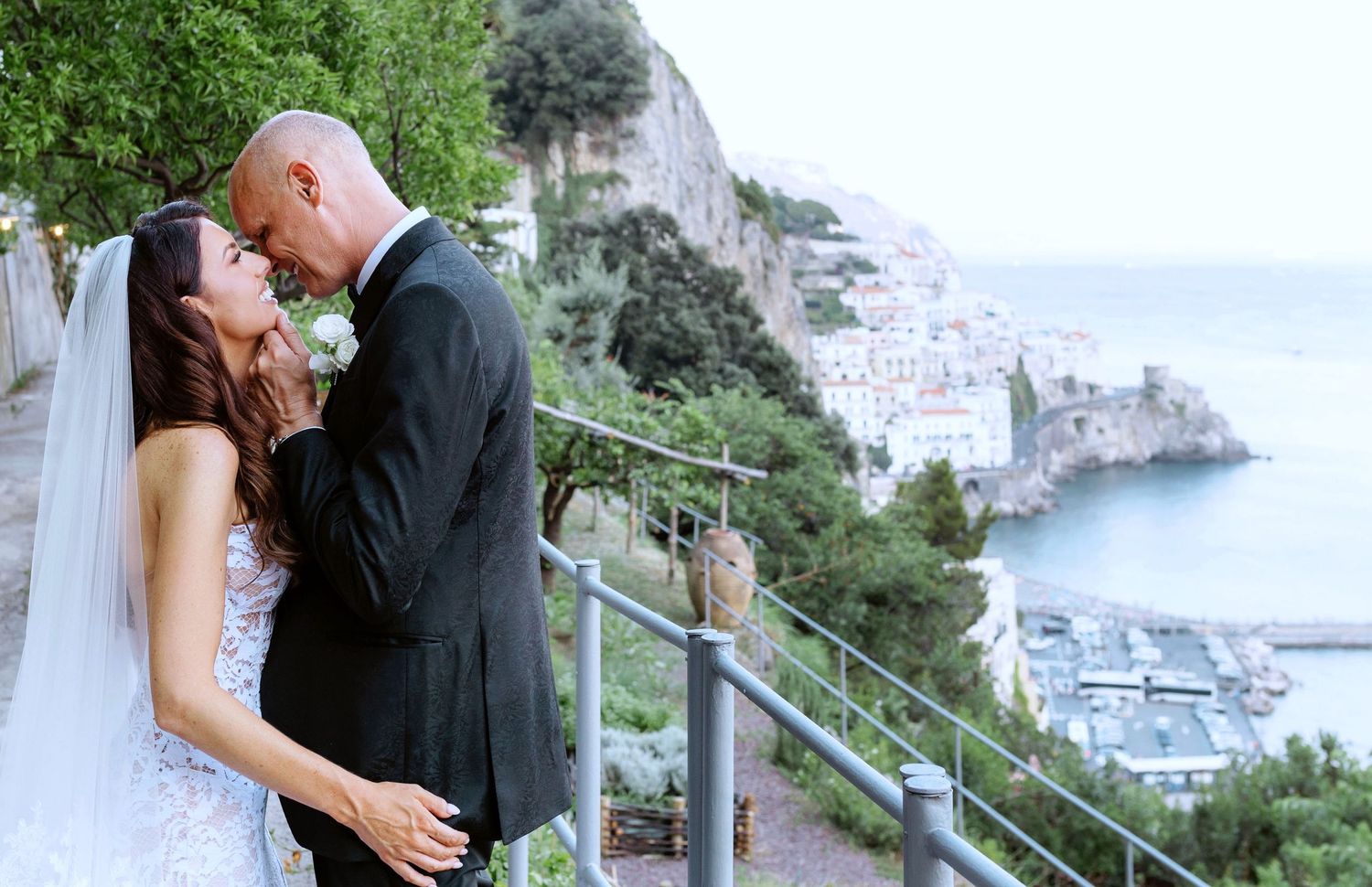 Bride and groom share a romantic moment on a scenic Amalfi Coast terrace with stunning cliffside village views.