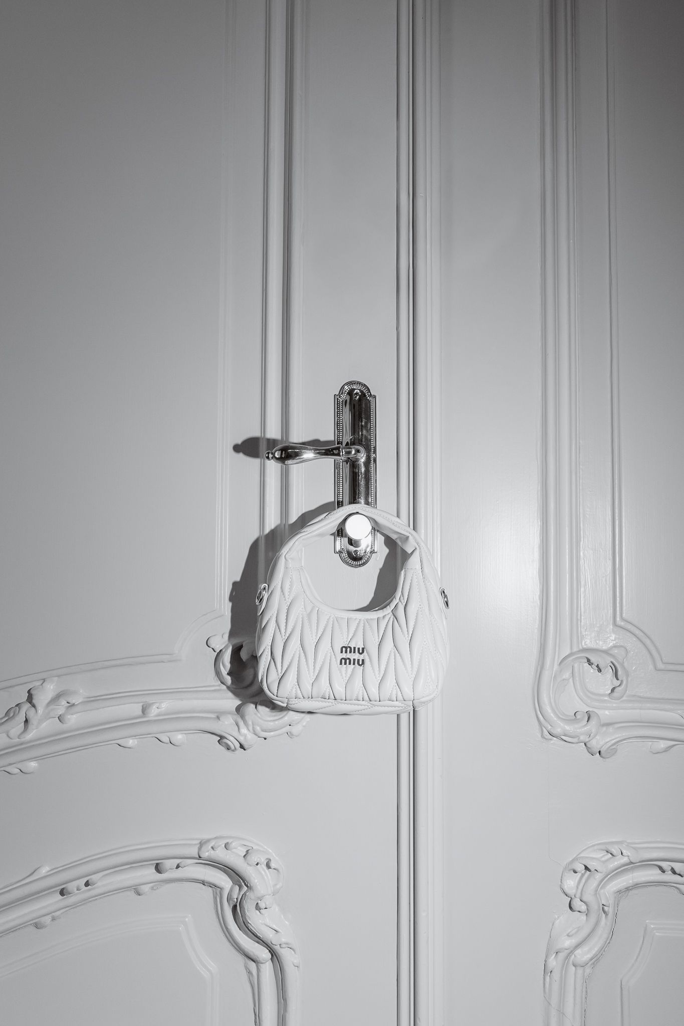 White Miu Miu quilted mini bag hanging on ornate white door handle in black and white.