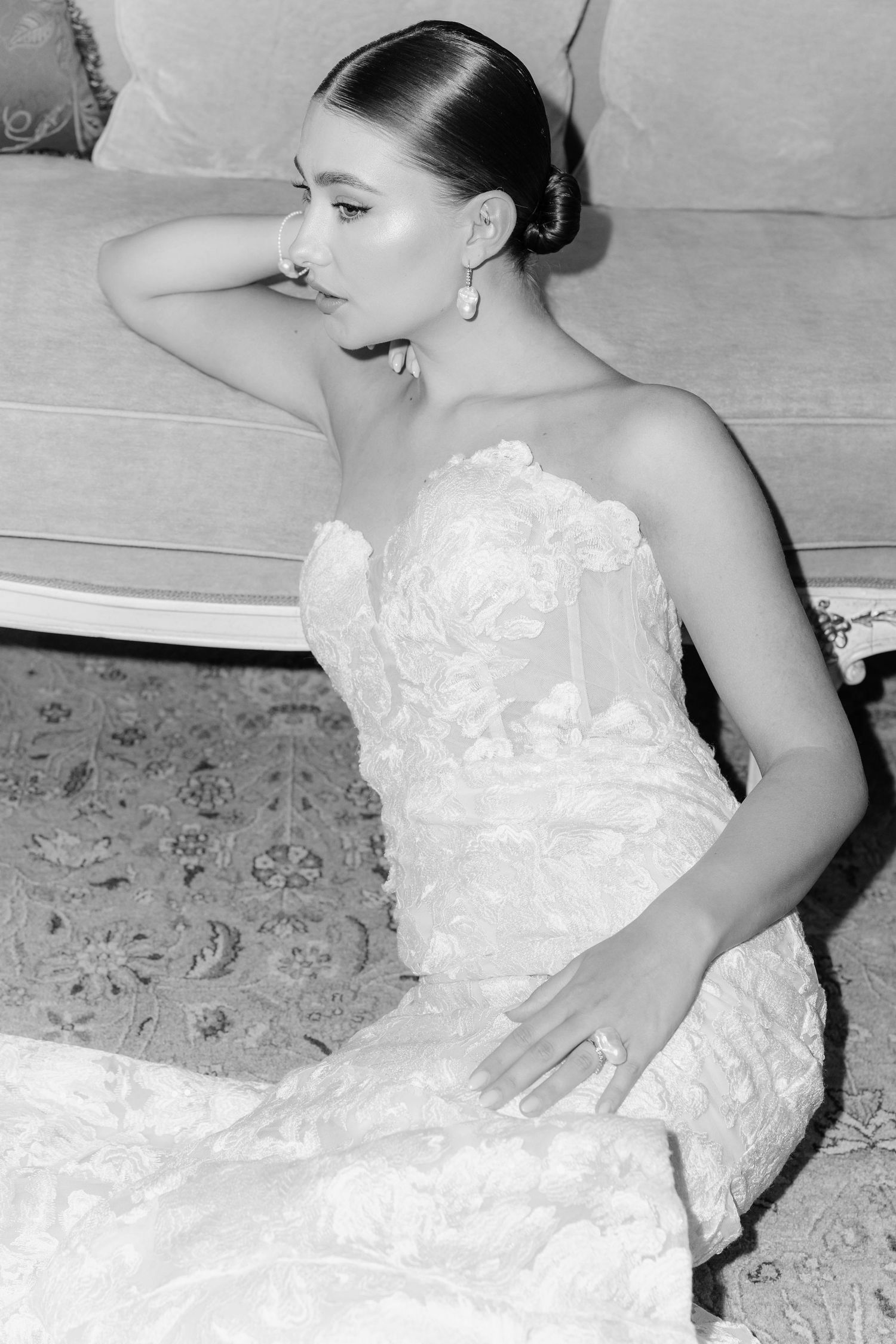Bride in strapless floral lace wedding gown poses gracefully on floor in black and white portrait in Vienna.