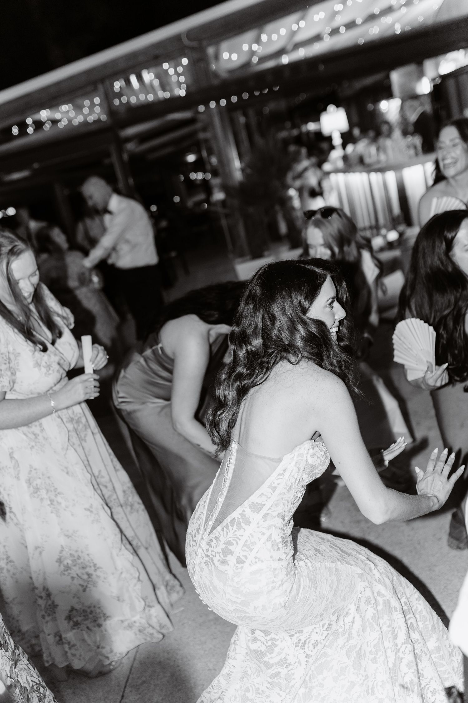 Black and white photo of bride dancing with guests at wedding reception party.