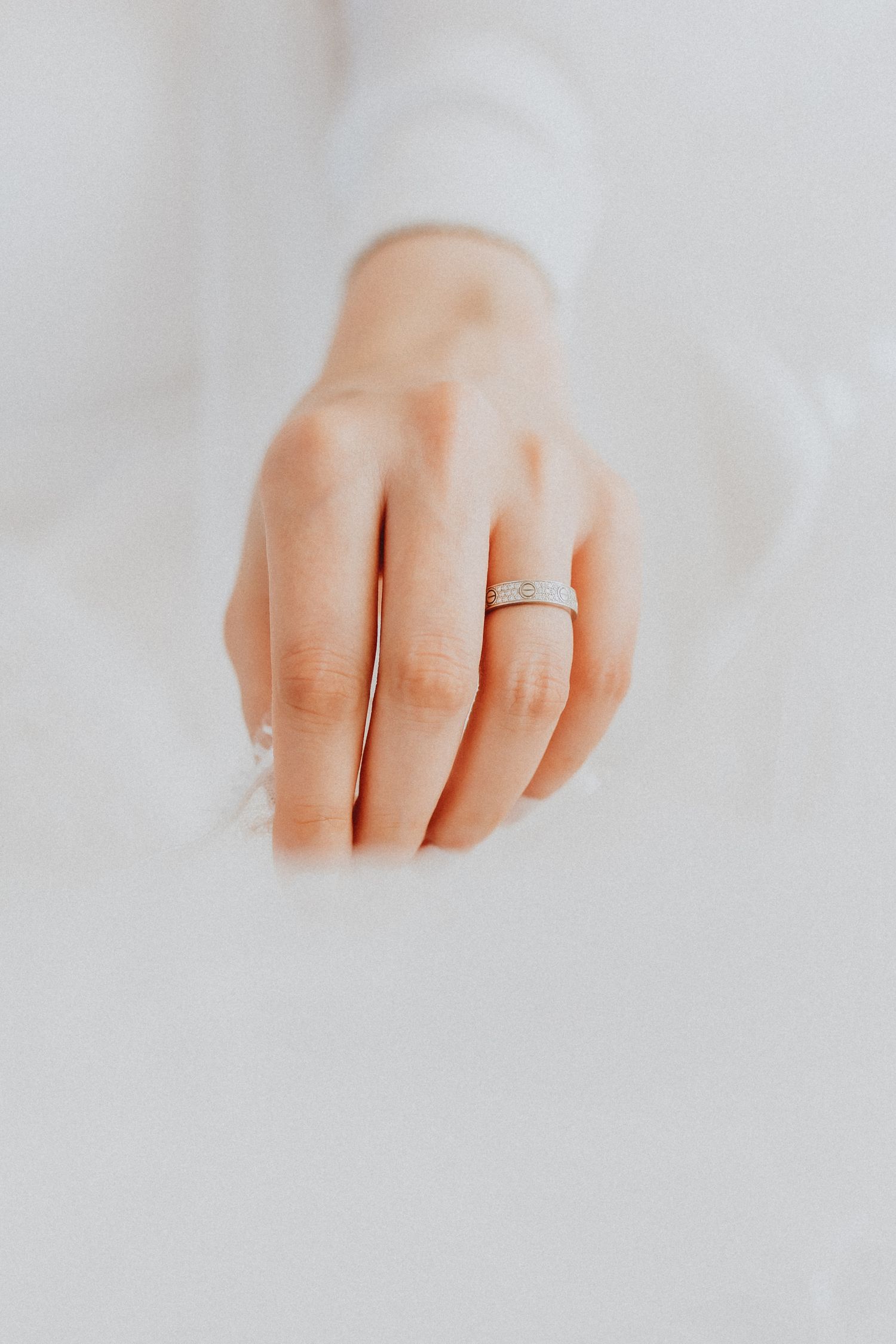 Close-up of a hand wearing a delicate silver diamond band ring against a soft white background.