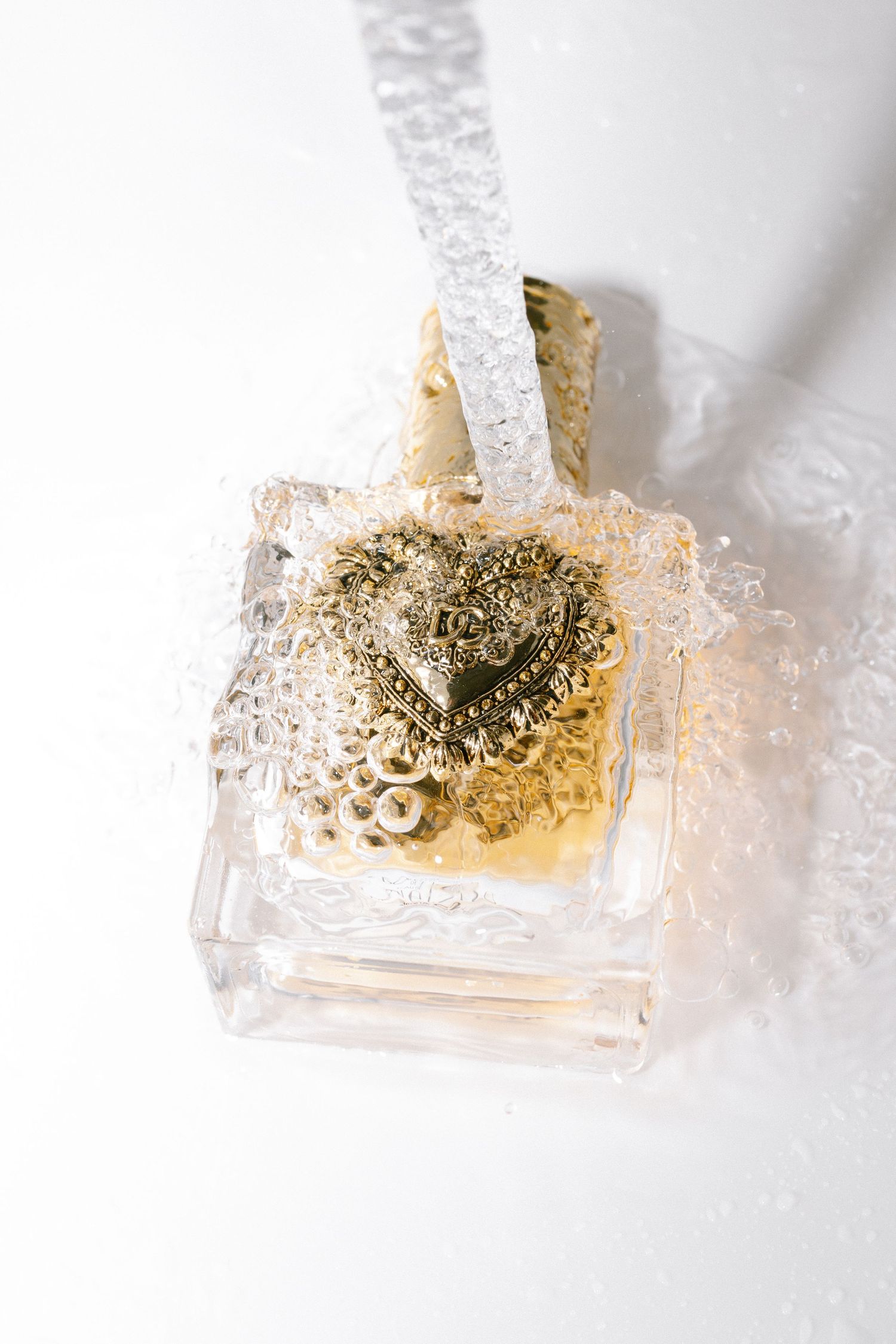 Gold heart embellished Juicy Couture perfume bottle with bubbles on white background.