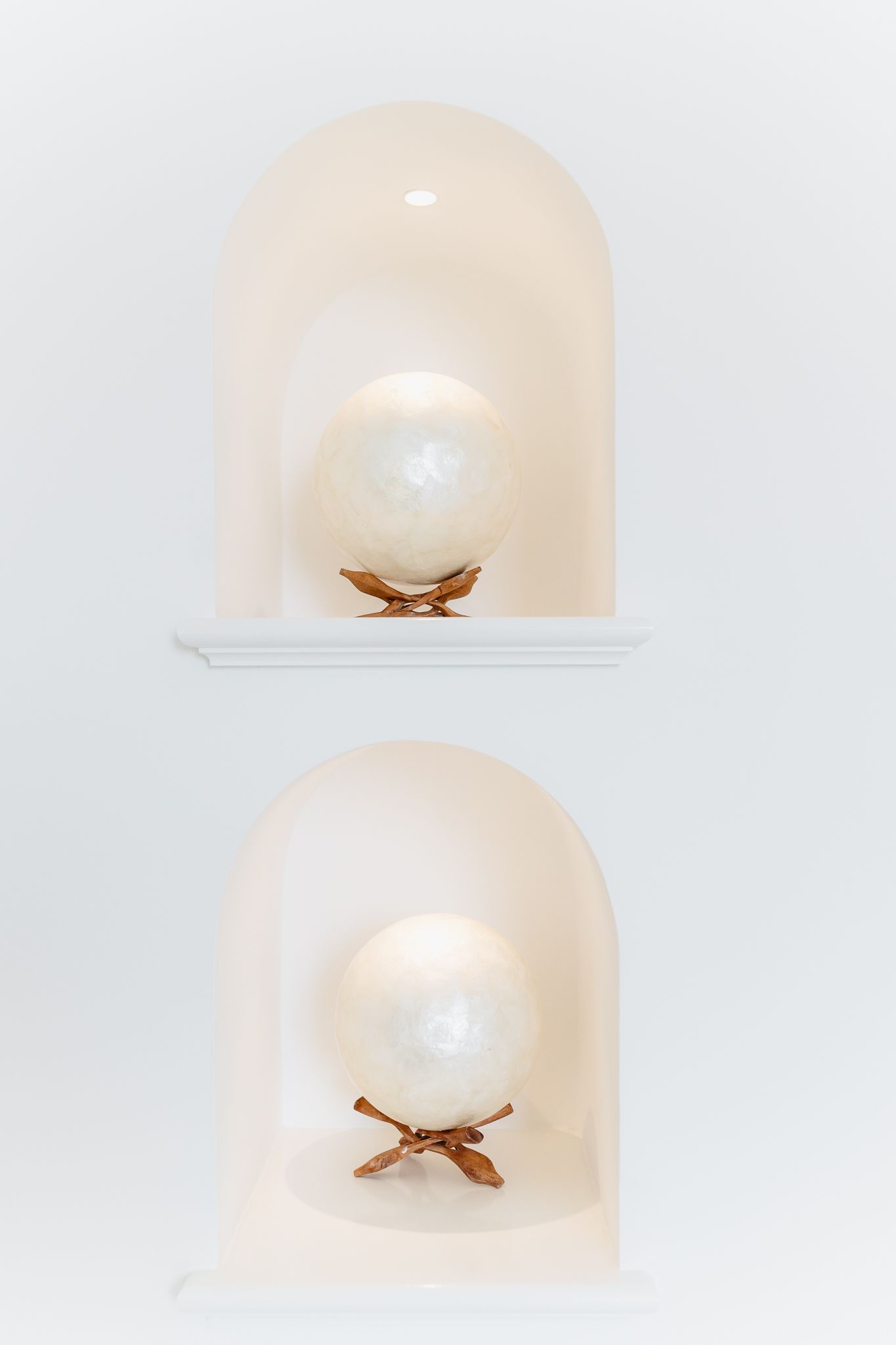 Two illuminated white arched niches displaying decorative pearl spheres on wooden stands.