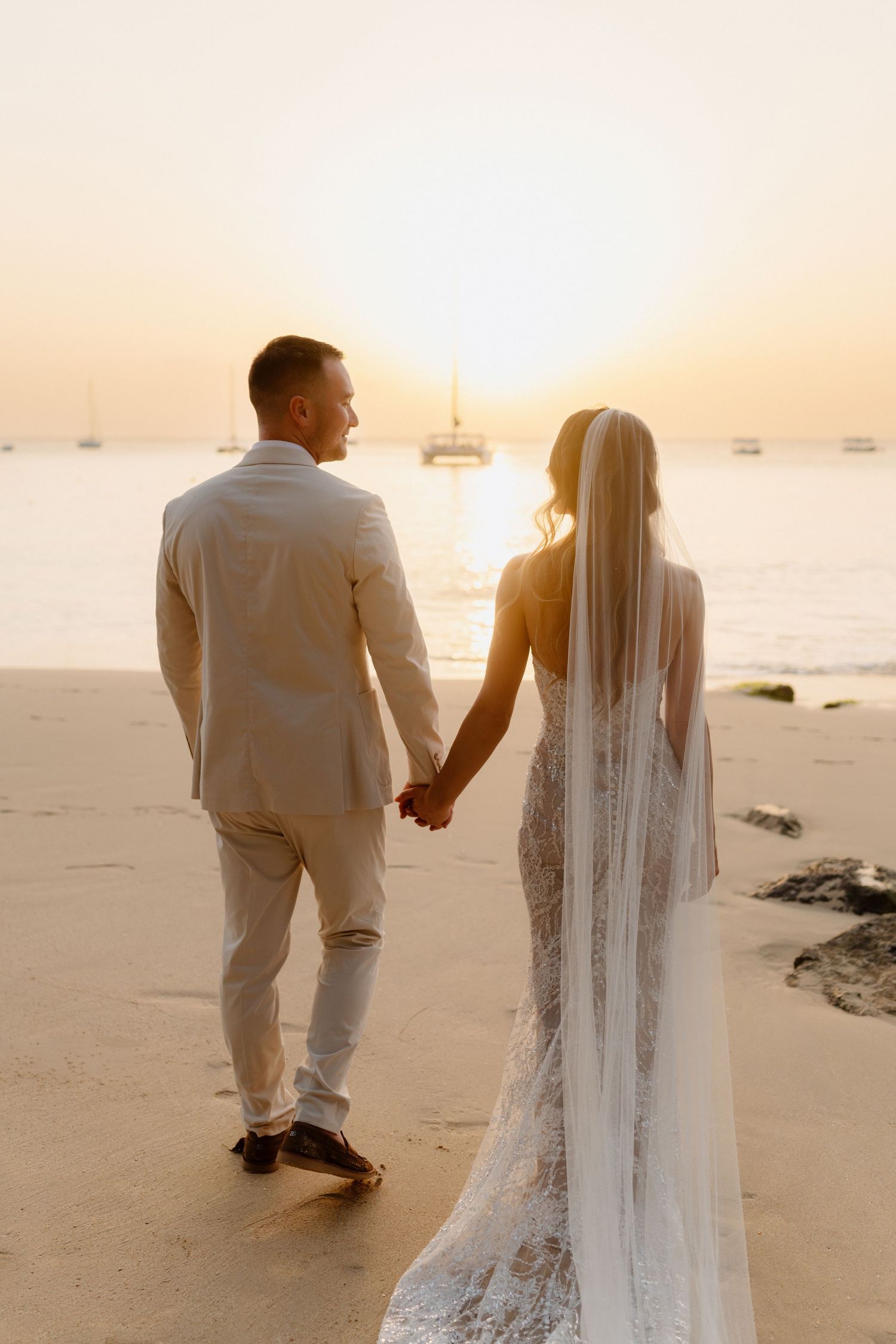Bride and groom holding hands walking toward a stunning ocean sunset on a sandy beach. Barbados photographer