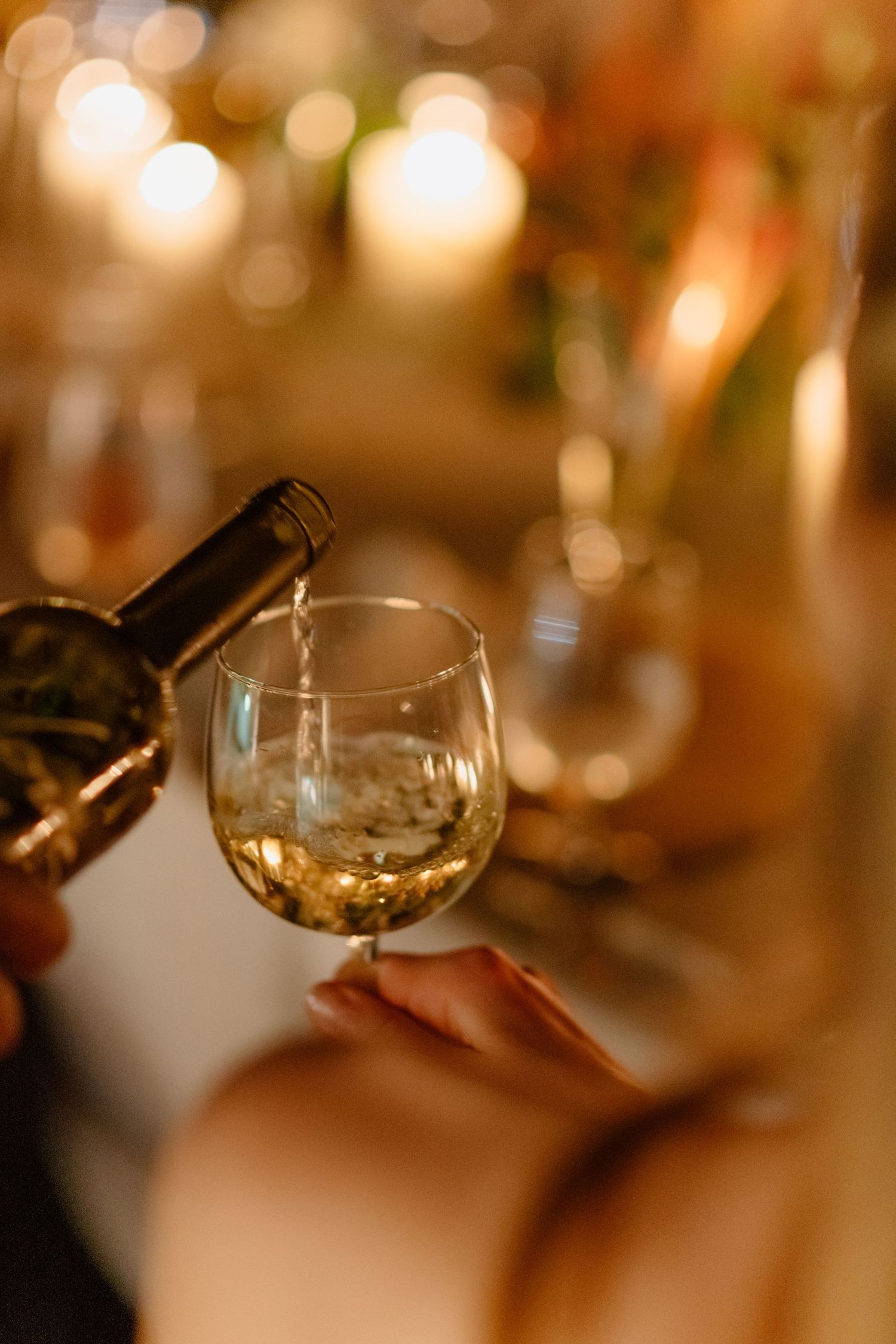 Close-up of white wine being poured into a stemless glass at a candlelit wedding reception. Barbados photographer