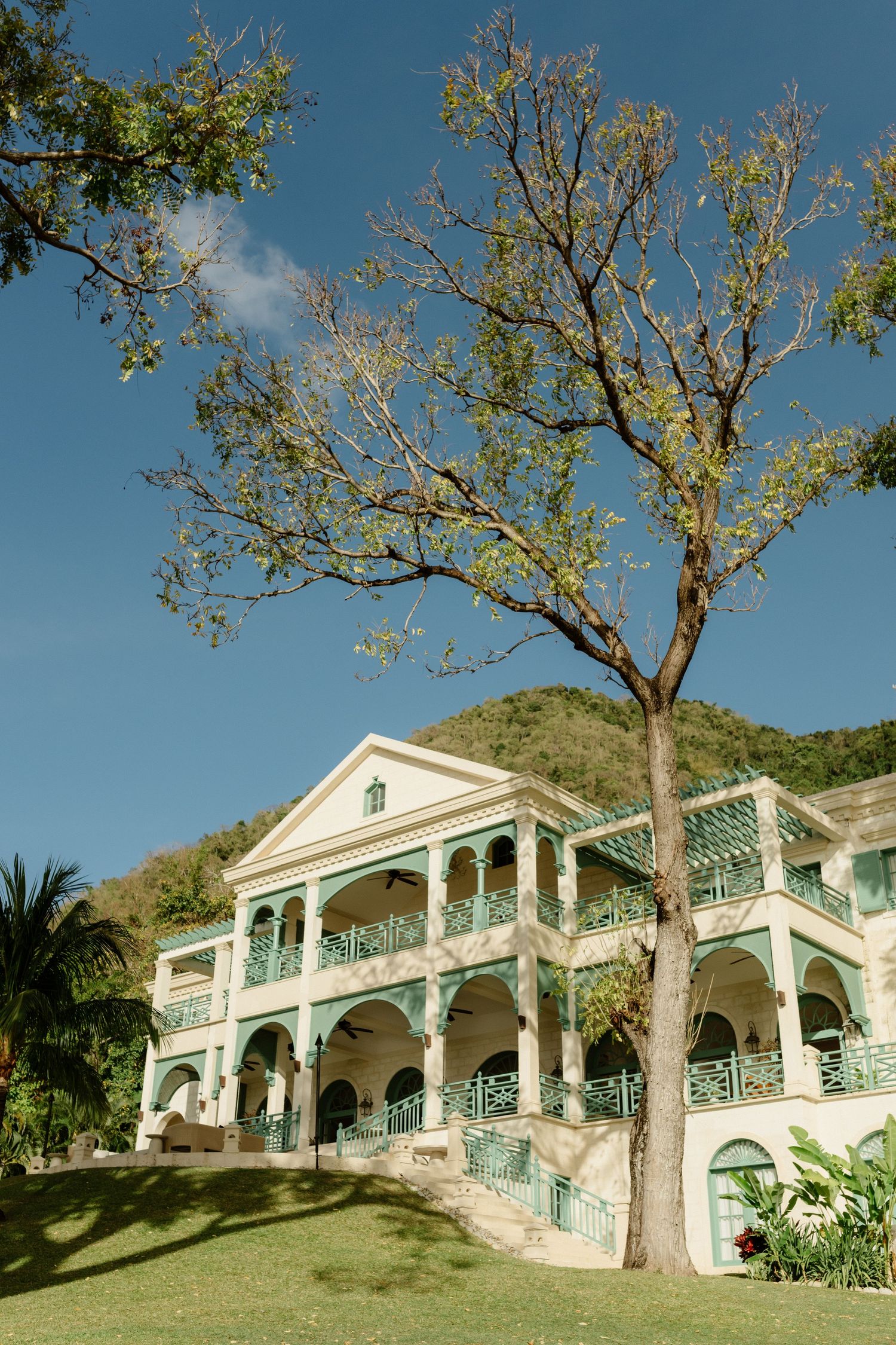 Grand two-story colonial estate with teal balconies and arches surrounded by tropical trees and hills. St Lucia Wedding photographer