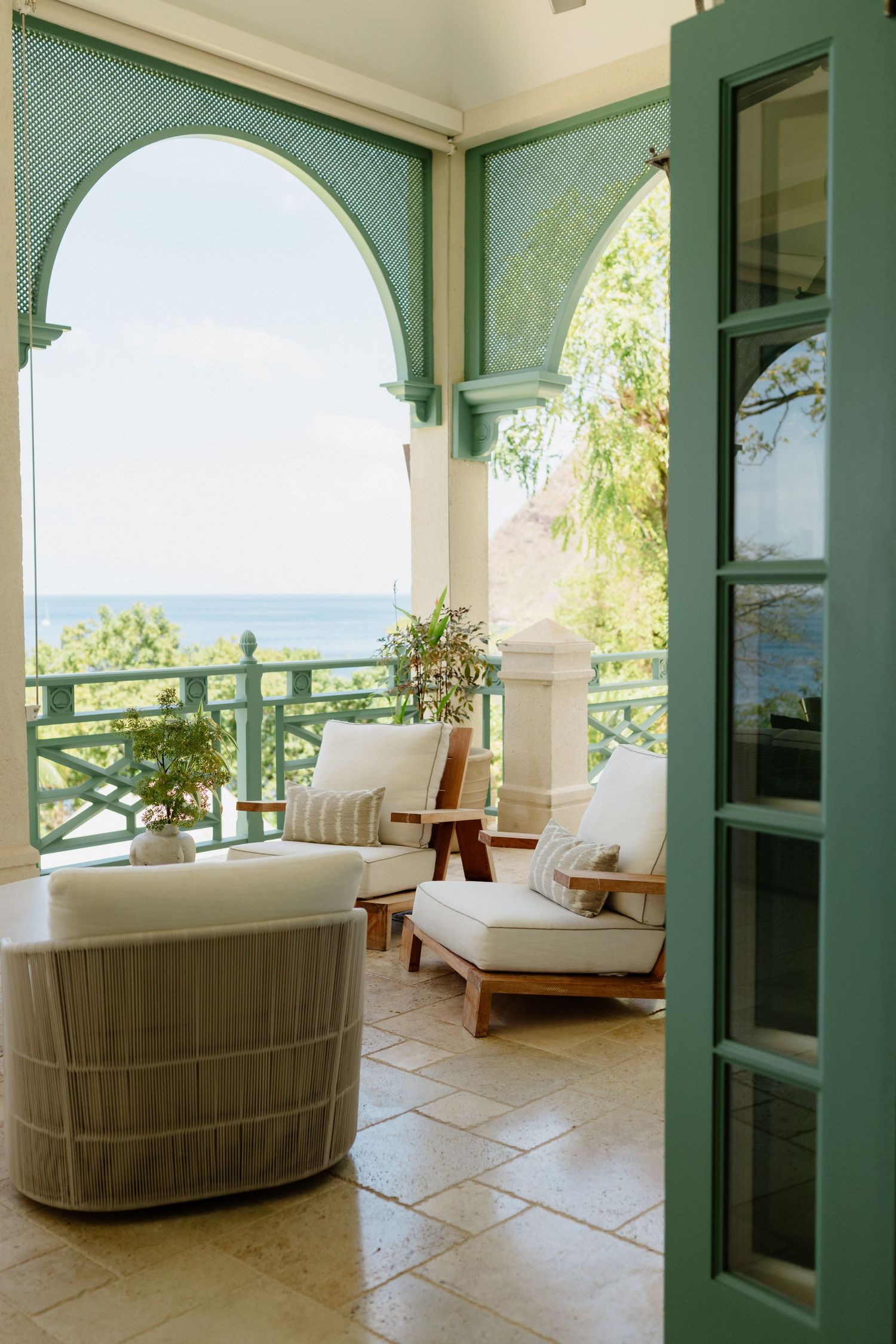 Serene resort veranda with white cushioned chairs, green arched columns, and ocean views. St Lucia Wedding photographer