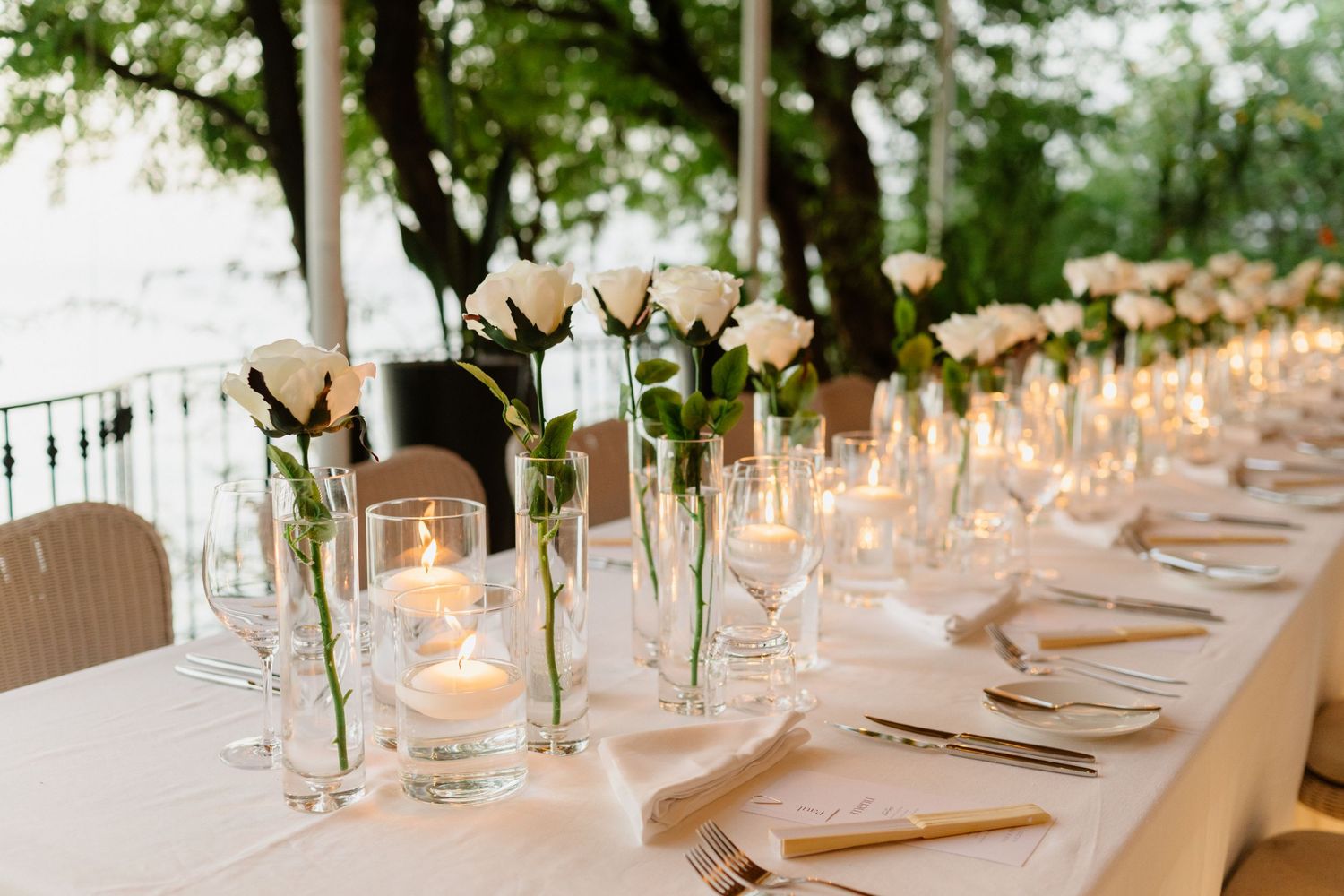 Elegant wedding reception table with white roses in glass vases and glowing candles set outdoors.  Barbados Destination Wedding Photographer