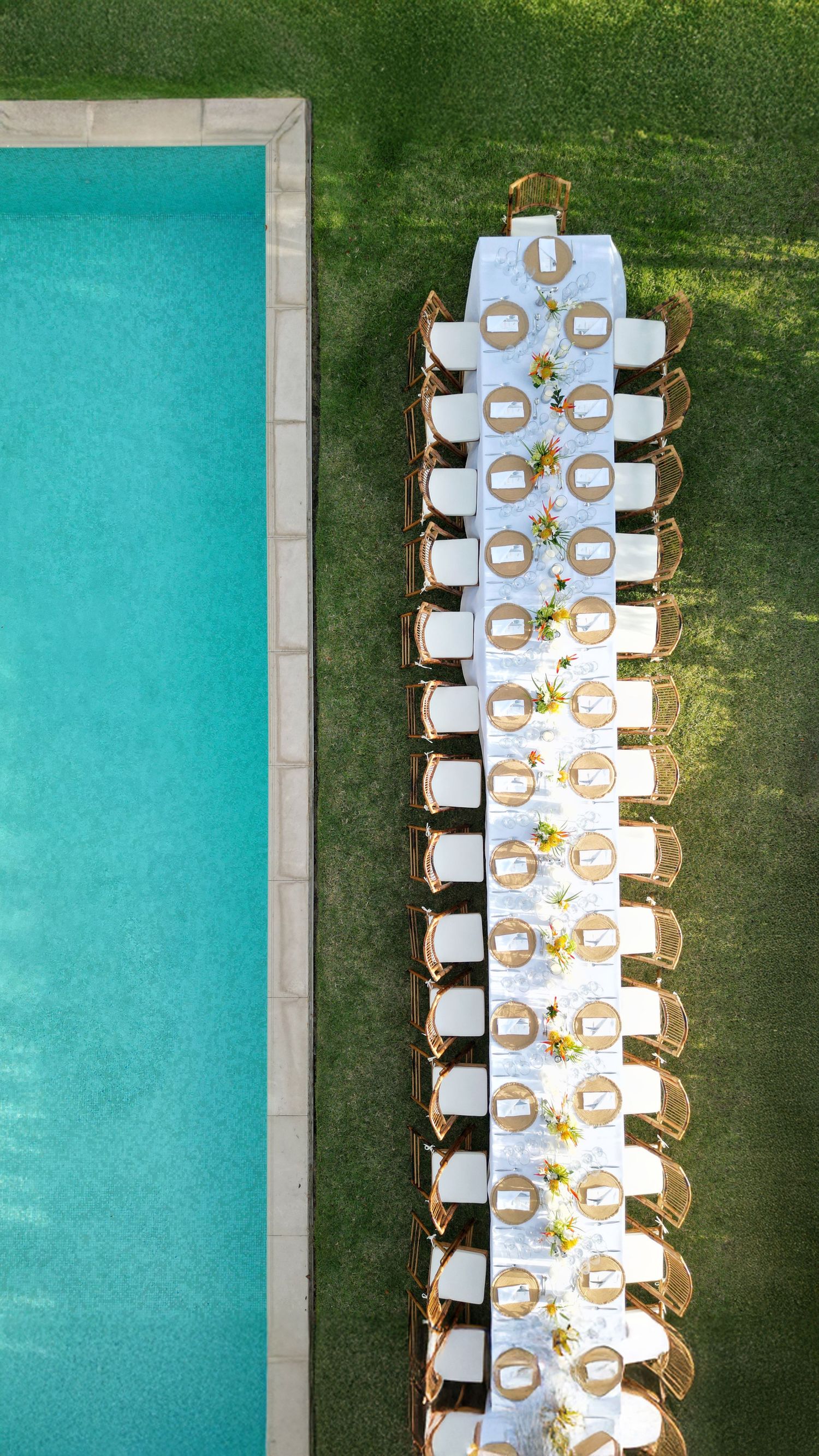 Aerial daytime view of a long wedding reception table set beside a turquoise swimming pool.  Barbados Destination Wedding Photographer
