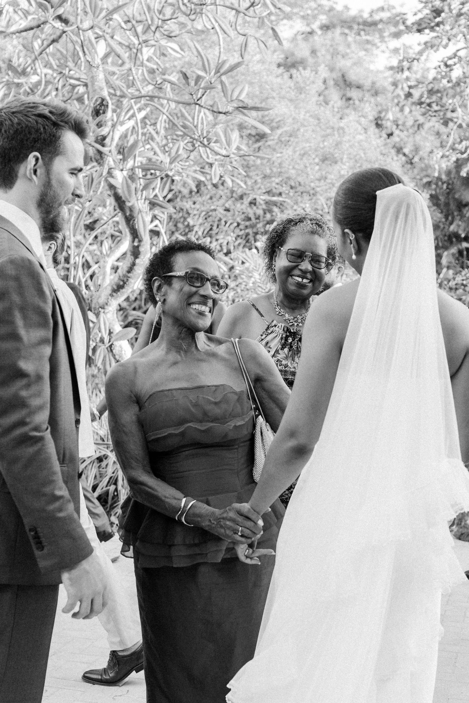 Black and white candid moment of smiling wedding guests greeting bride during outdoor ceremony. Barbados photographer