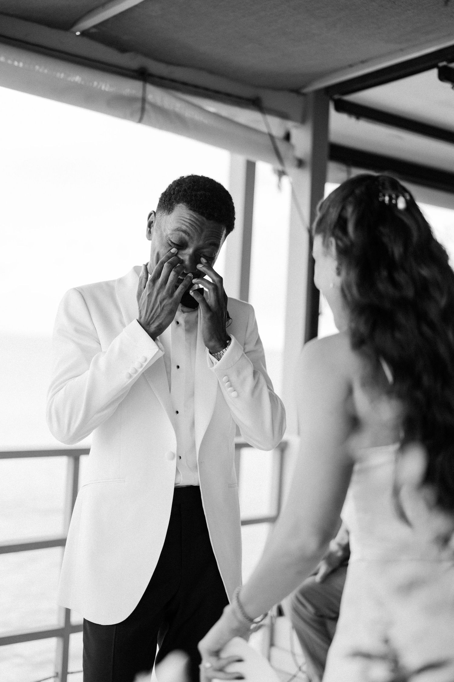 Emotional groom in white tuxedo wipes tears during touching outdoor wedding ceremony exchange. Barbados Destination Wedding Photographer