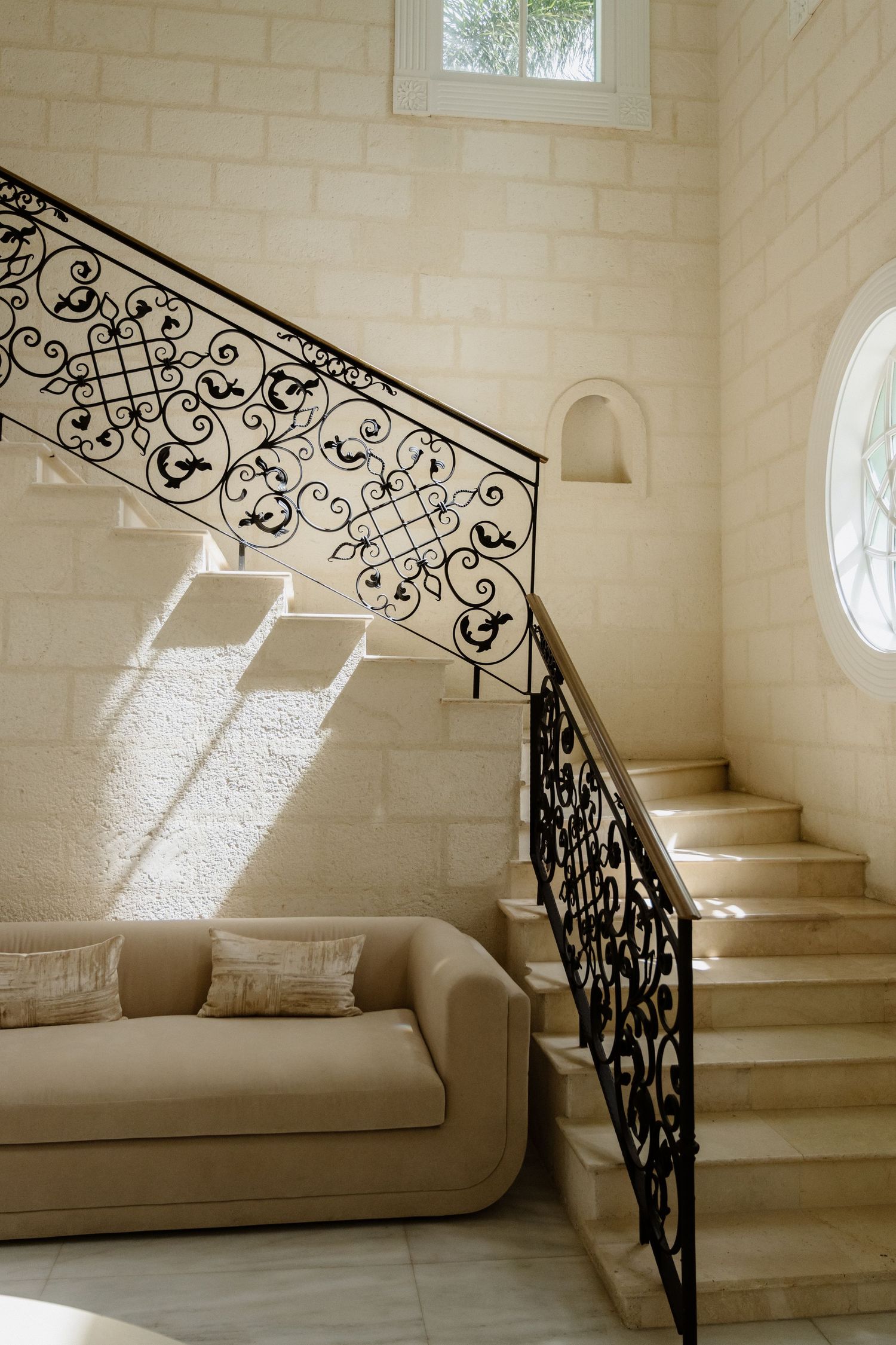 Elegant staircase with ornate black wrought iron railing beside a beige sofa in a limestone interior. St Lucia Wedding photographer