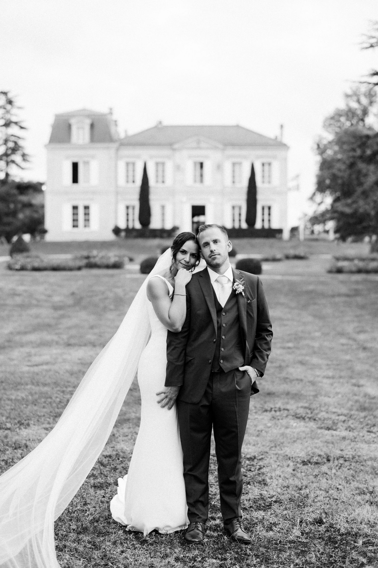 Black and white portrait of bride and groom standing before an elegant French chateau estate. Barbados Destination Wedding Photographer