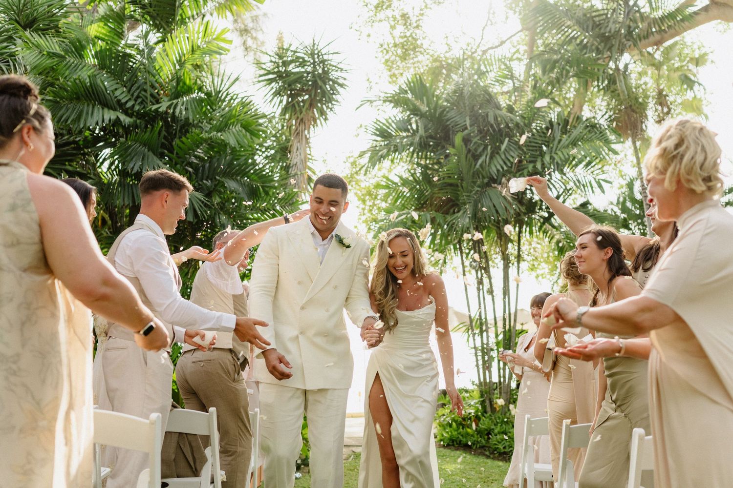 Joyful newlyweds in ivory outfits celebrate recessional with cheering guests at tropical wedding. Barbados Destination Wedding Photographer