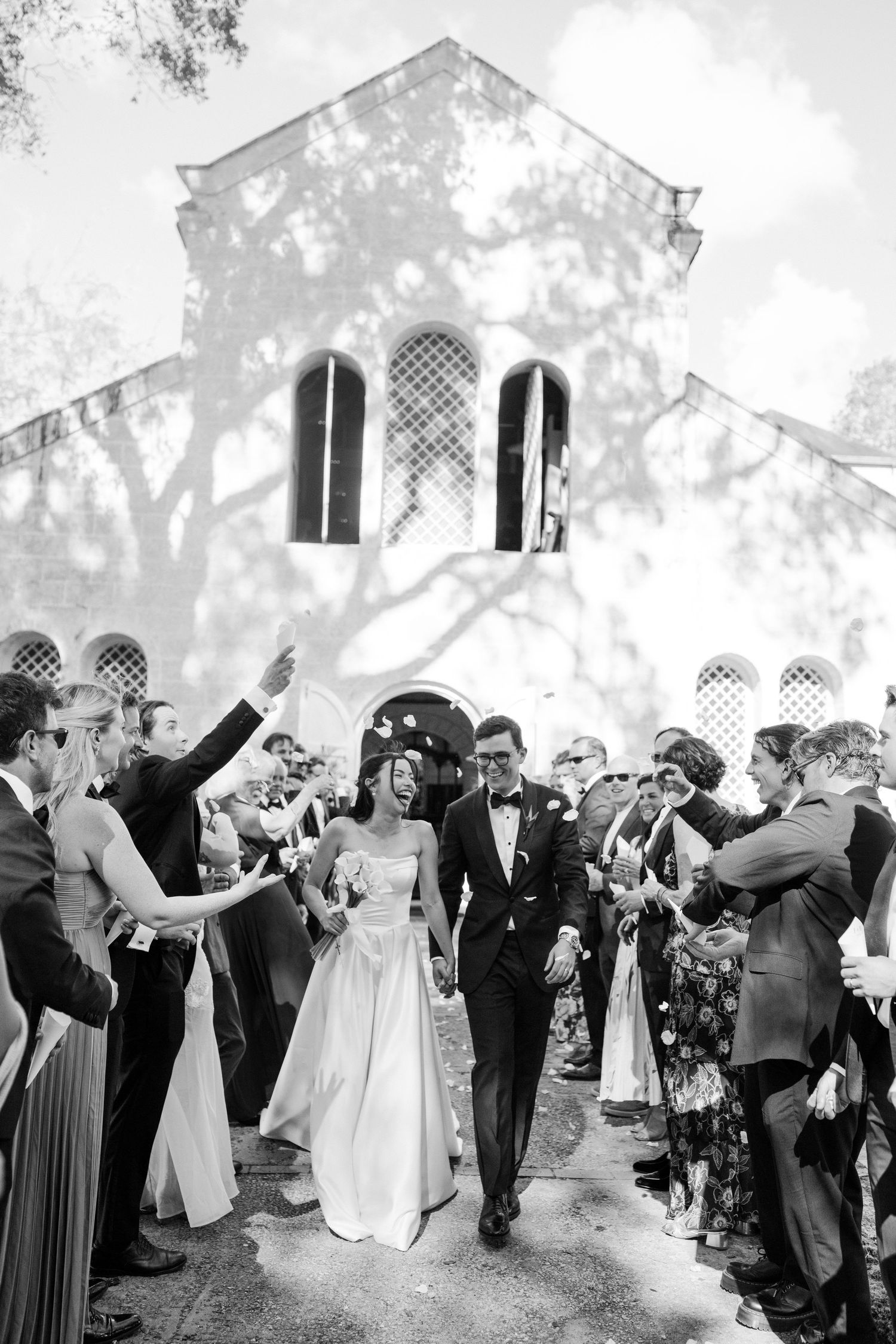 Bride and groom exit historic church surrounded by cheering guests in classic photo. Barbados Destination Wedding Photographer