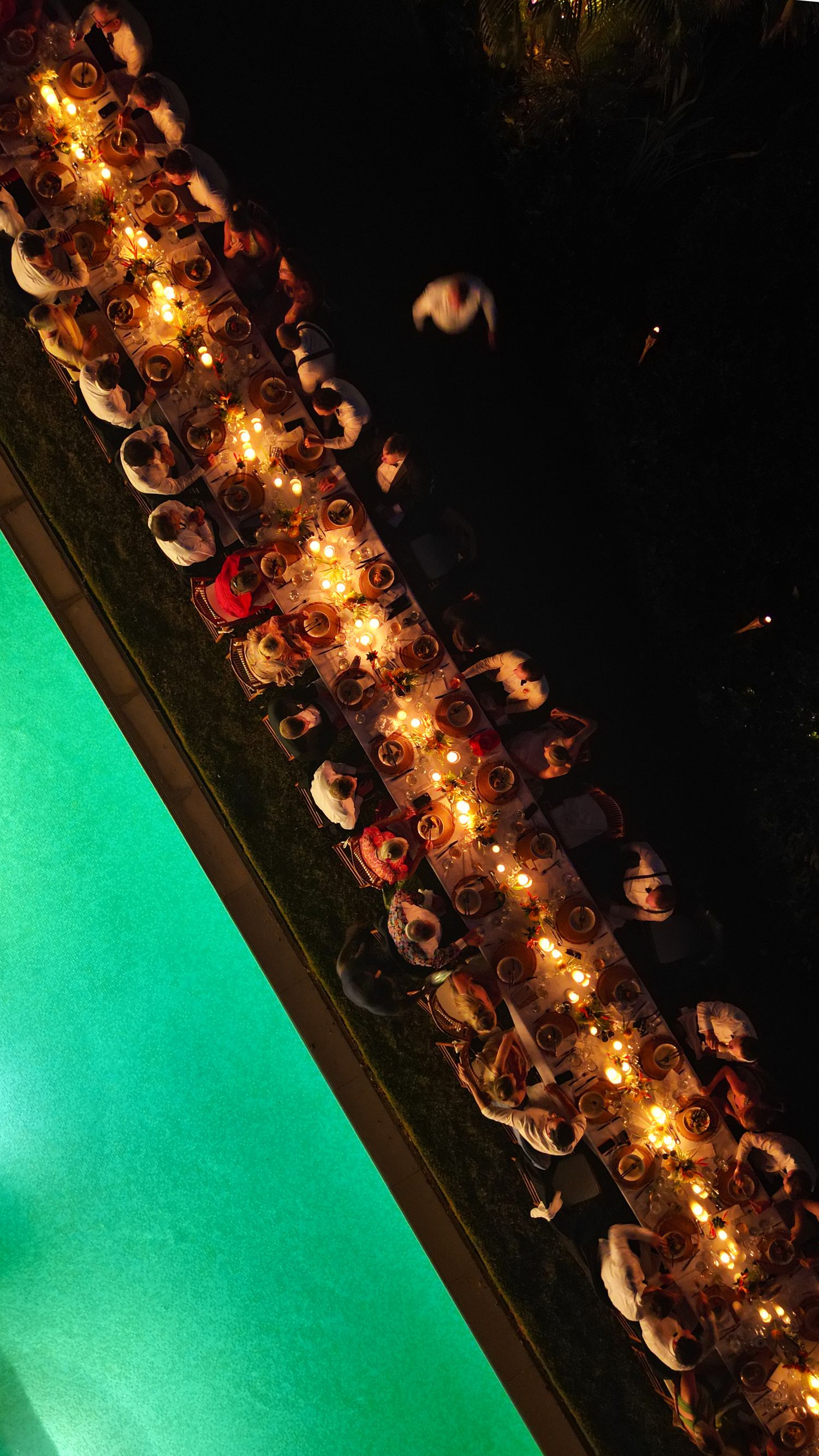 Aerial night view of a long illuminated wedding reception table beside a glowing green pool. Barbados Destination Wedding Photographer